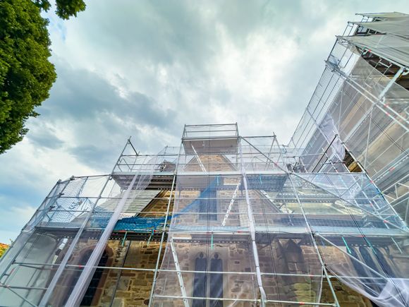 Église sous échafaudages, recouverte de filets, ciel nuageux.