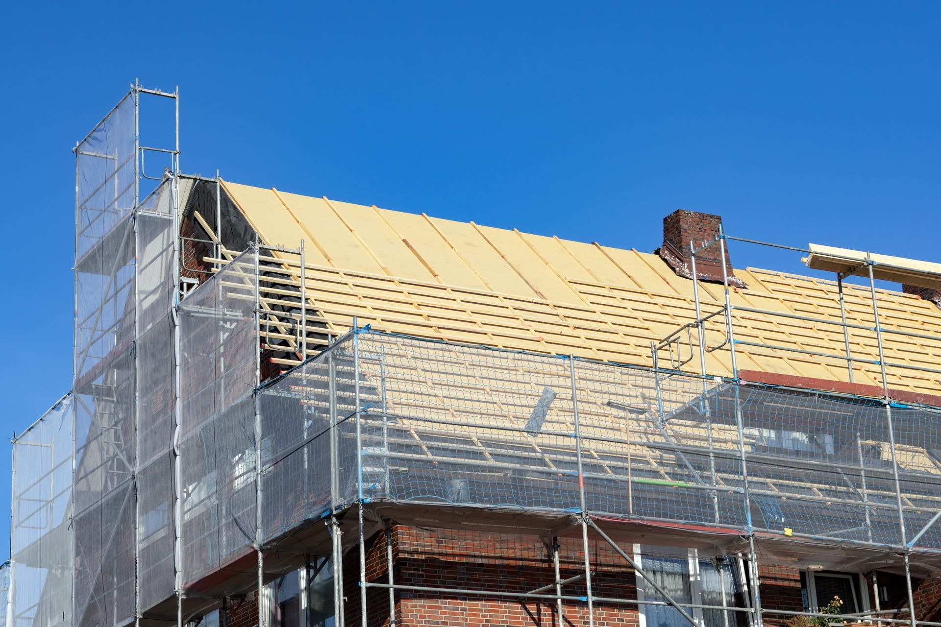 Bâtiment au toit partiellement construit, recouvert d'échafaudages et de filets de sécurité, se détachant sur un ciel bleu clair.