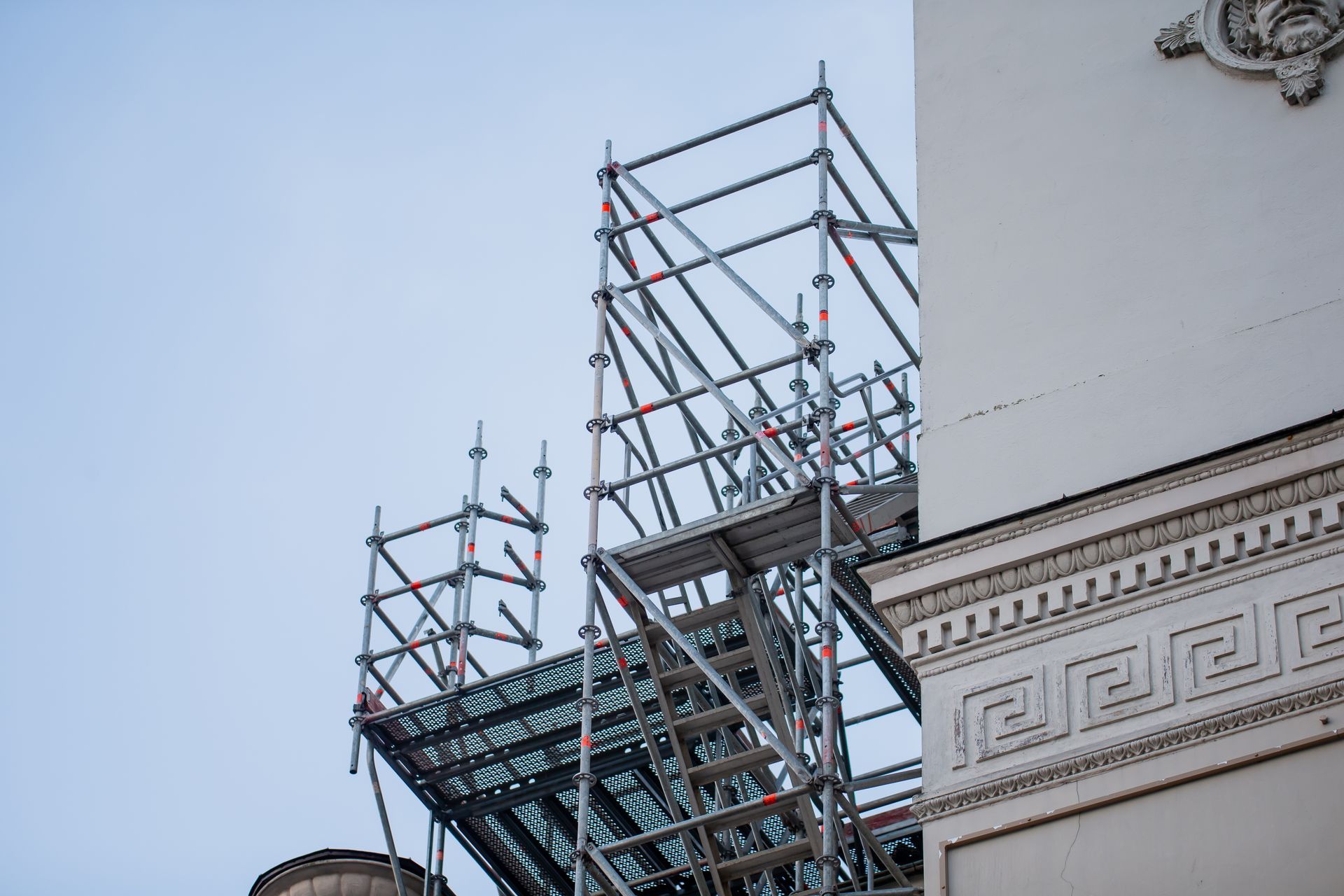 Des échafaudages sont installés autour d'un bâtiment en pierre sous un ciel bleu, probablement pour des travaux de construction.
