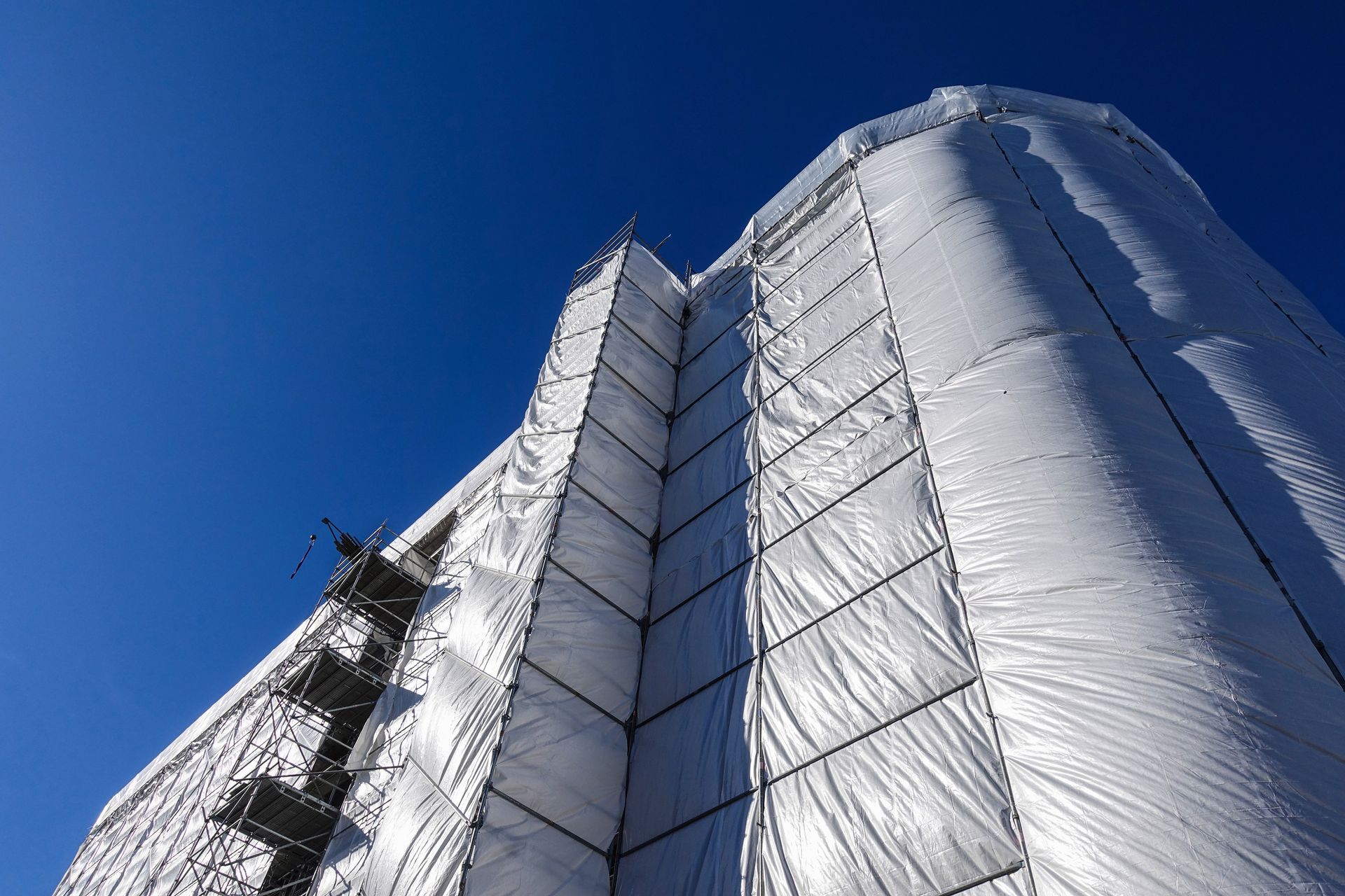 Bâtiment recouvert de bâches blanches, avec des échafaudages se détachant sur un ciel d'un bleu éclatant.