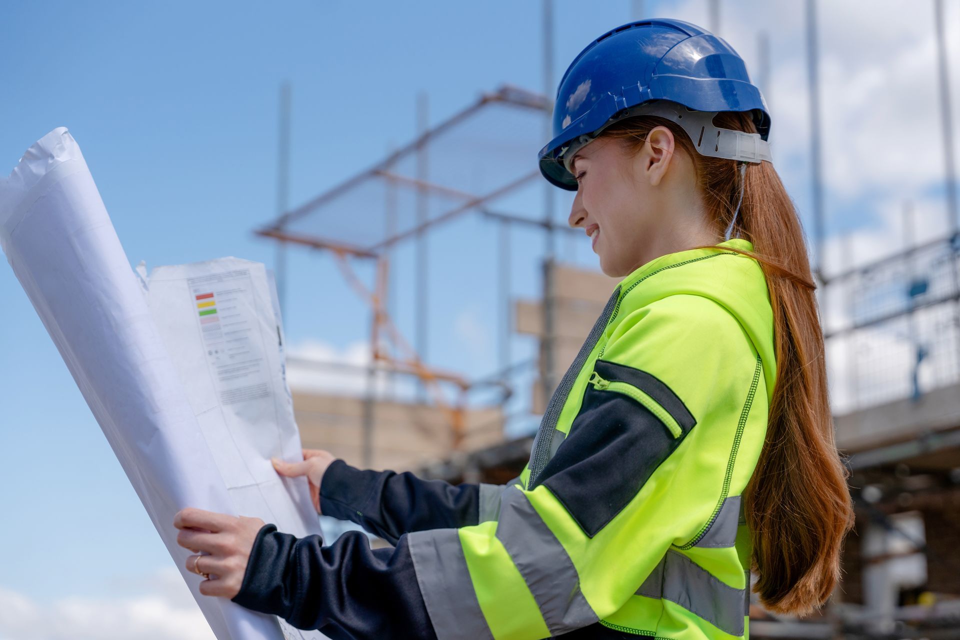 Ouvrier du bâtiment portant un casque bleu examinant des plans sur un chantier.