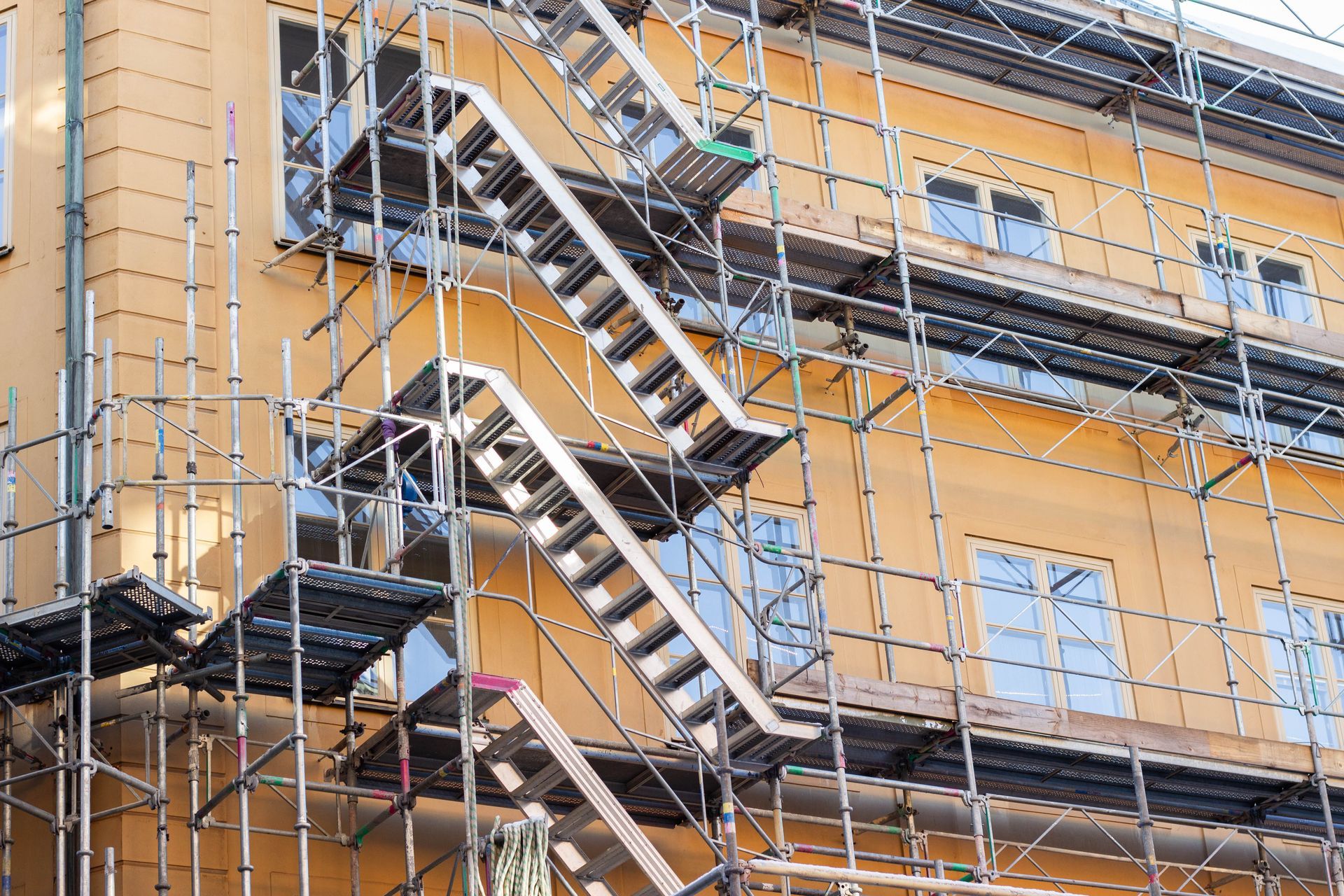 Façade orange du bâtiment avec escaliers de secours métalliques extérieurs derrière une clôture grillagée