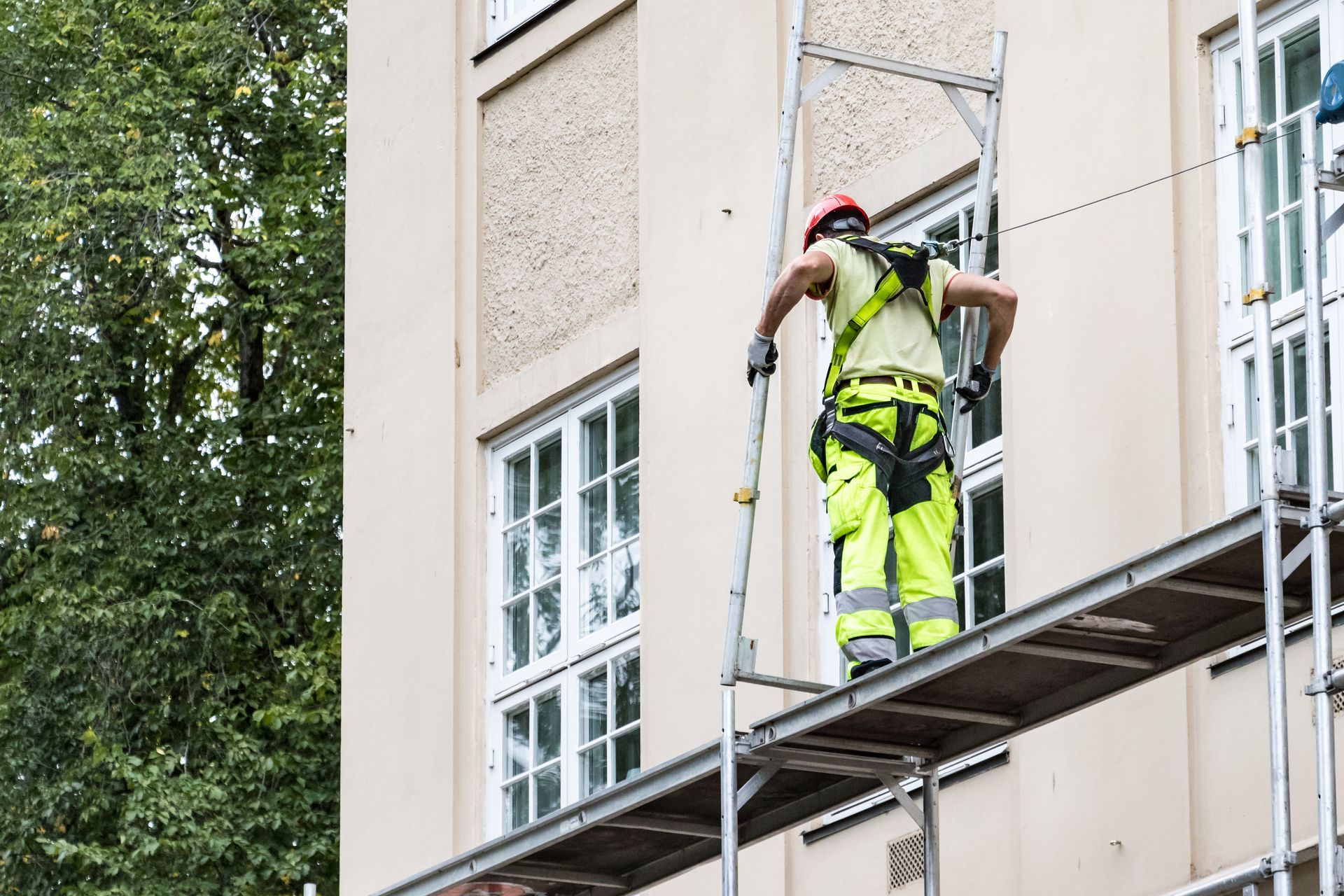 Ouvrier du bâtiment sur un échafaudage, portant un harnais de sécurité, à côté d'un bâtiment.