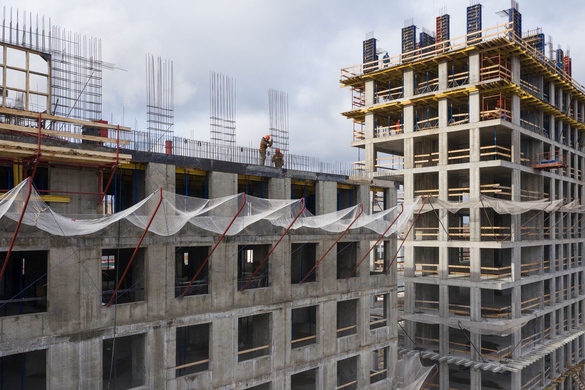 Construction d'immeubles en béton de plusieurs étages. Des ouvriers travaillent sur le toit sous un ciel nuageux.