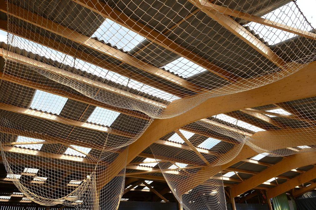 Des ouvriers à bord de nacelles élévatrices installent des filets rouges sur la structure d'un bâtiment moderne.