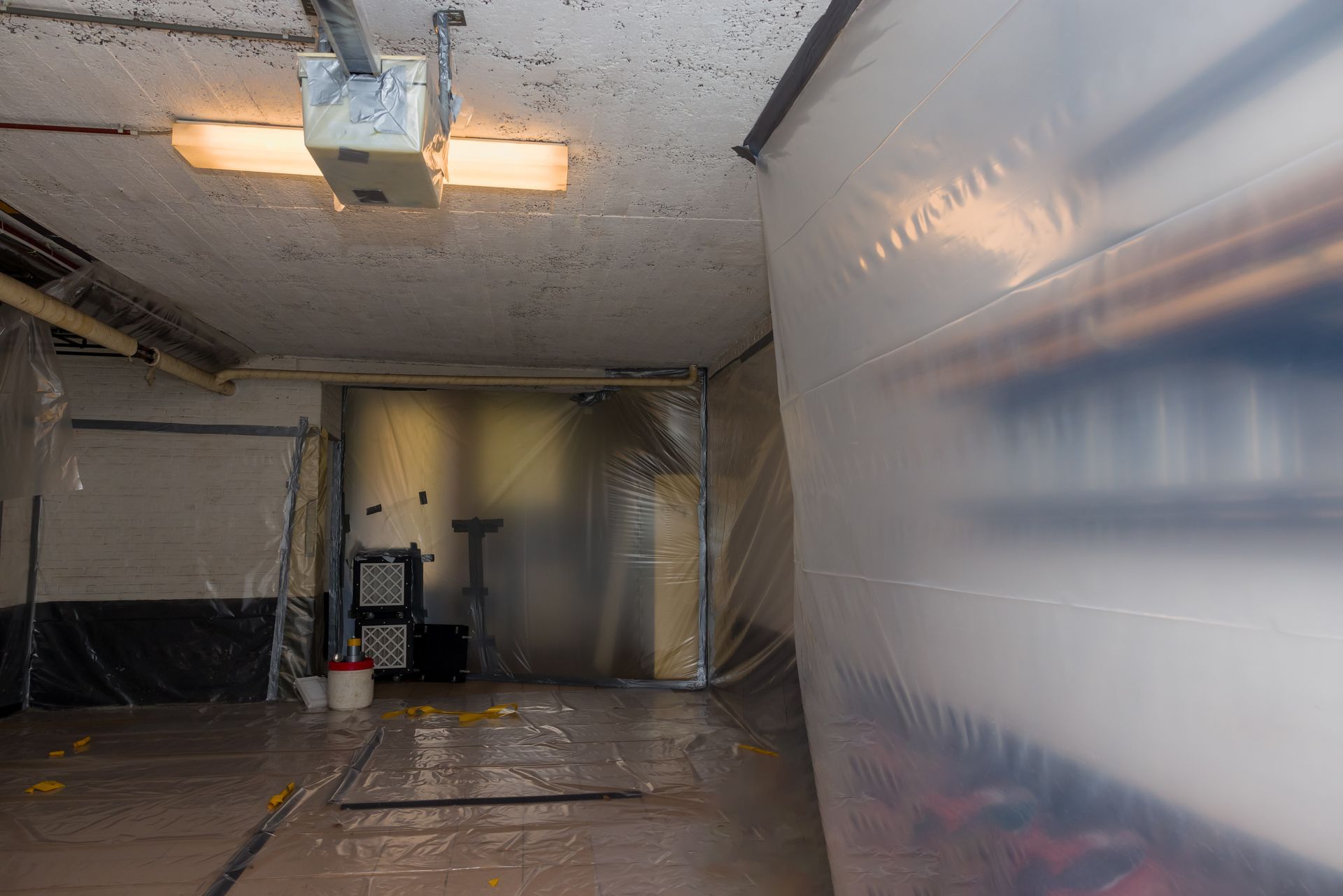 Intérieur du garage recouvert de bâches en plastique, probablement pour contenir les dégâts pendant les travaux de rénovation ou de nettoyage.