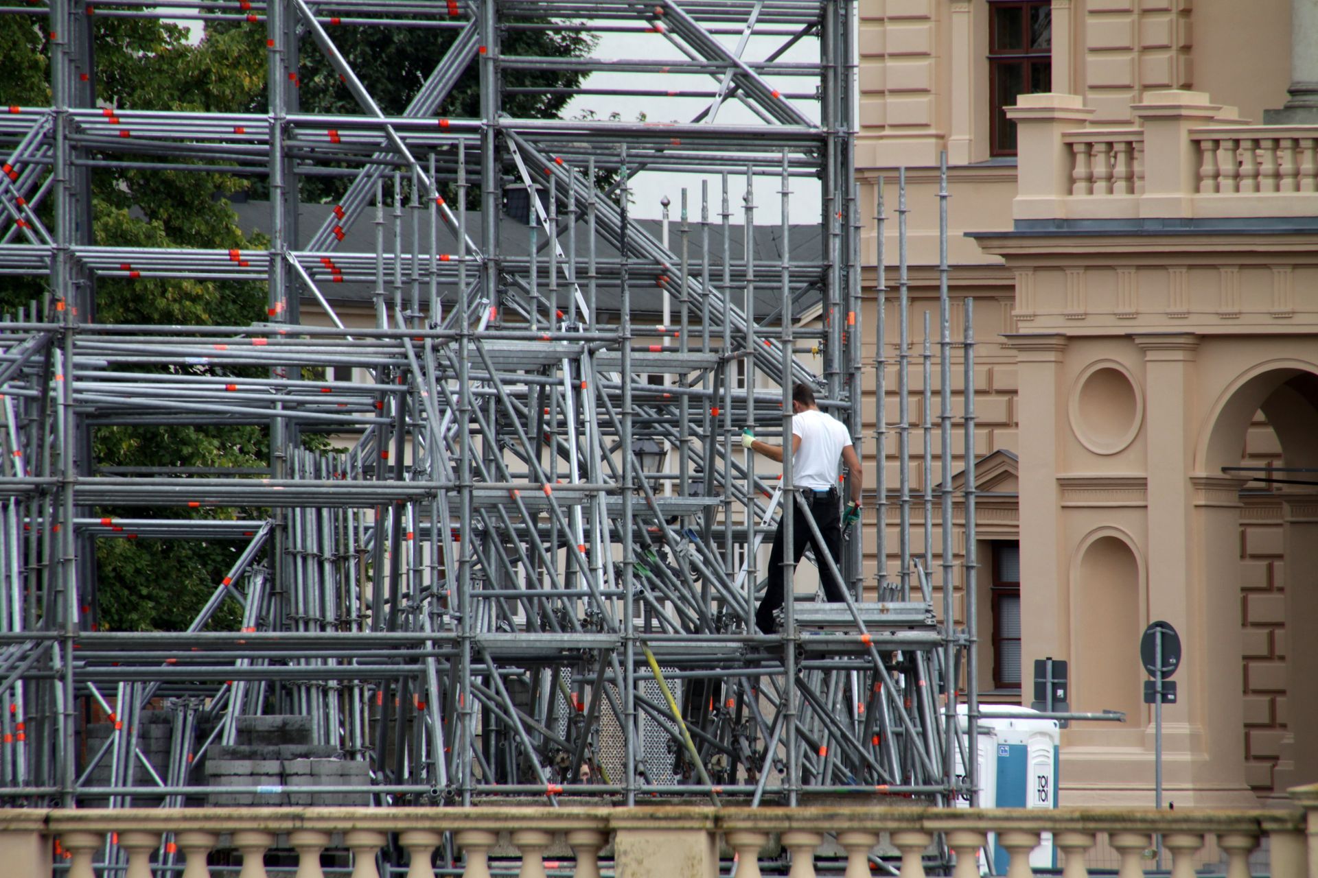 Ouvrier sur un échafaudage à côté d'un bâtiment clair.