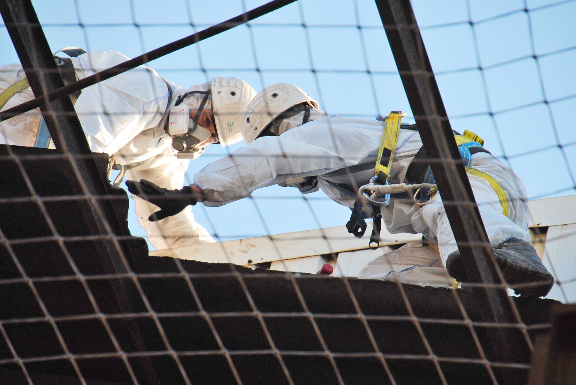 Bâtiment recouvert de matériaux blancs, chantier de construction, conteneurs rouges, ascenseur jaune, montagnes en arrière-plan.