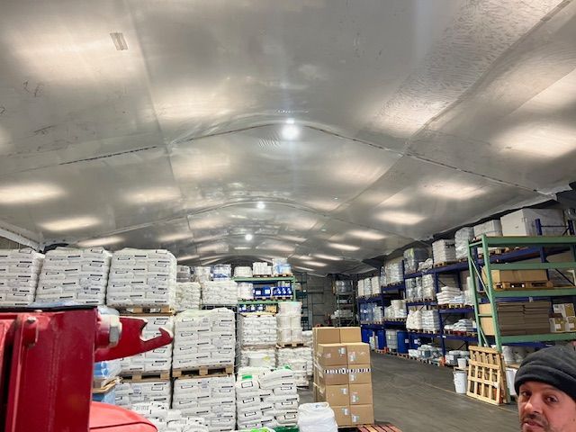 L'intérieur du bâtiment est recouvert de bâches en plastique blanc. Des poutres métalliques soutiennent un plafond haut et incliné.