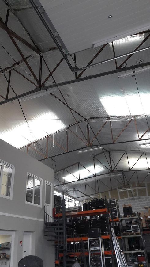 Intérieur d'un entrepôt à haute toiture métallique. On aperçoit des rayonnages d'équipements ainsi que des bureaux.