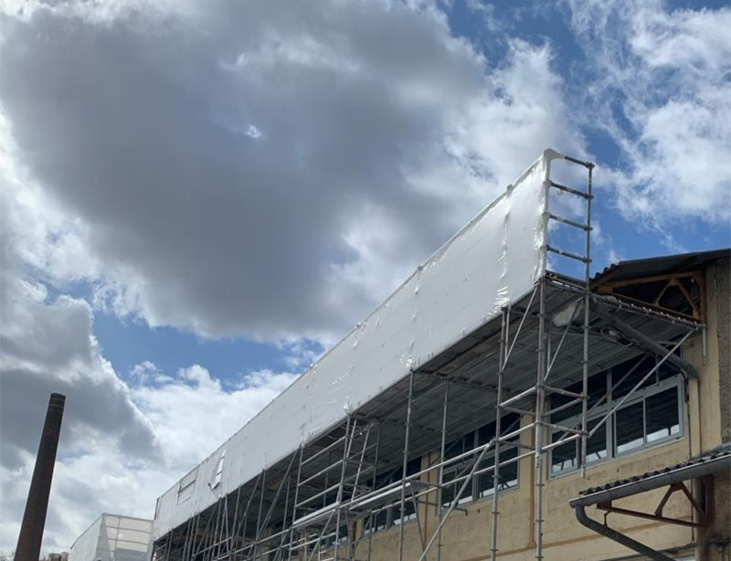 Une grande pièce vide aux murs blancs, avec un sol en béton, une ventilation et une porte.