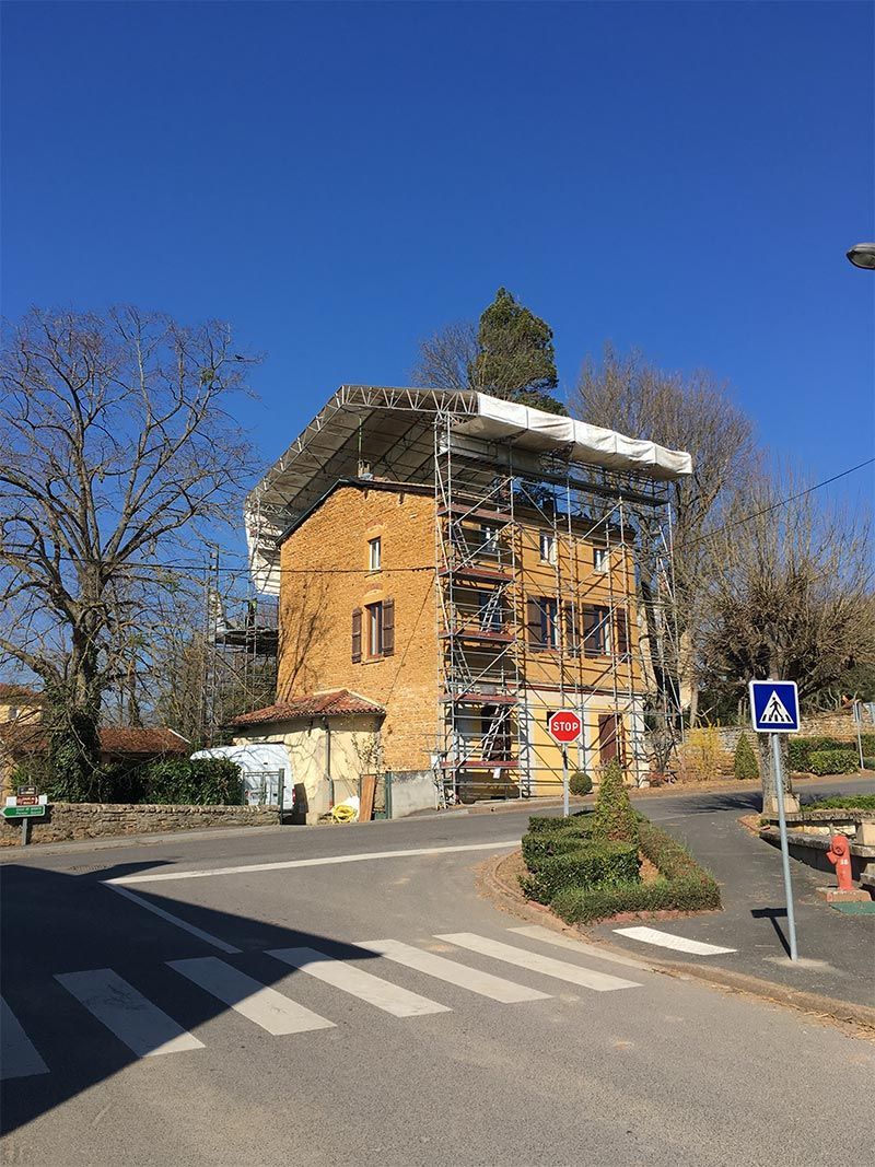 Bâtiment en briques avec échafaudages à un coin de rue, ciel bleu au-dessus, passage piéton au premier plan.