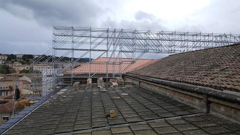 Échafaudage installé sur un toit de tuiles pour des travaux d'entretien du bâtiment sous un ciel nuageux.