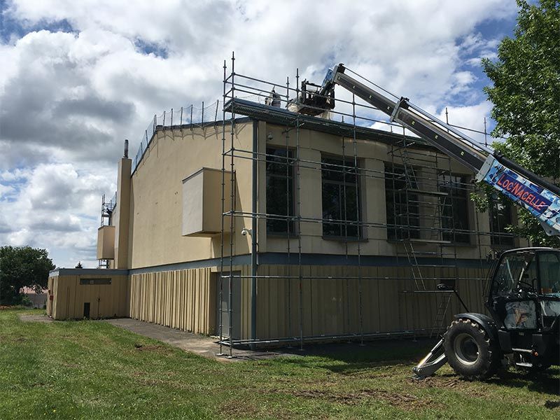 Bâtiment en construction, avec échafaudages et ascenseur. Ciel couvert.