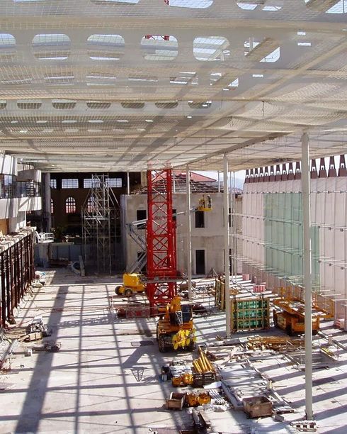 Chantier de construction avec grue rouge, engins jaunes et charpente métallique apparente.