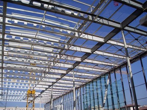 La structure métallique d'un bâtiment en construction, avec des murs de verre et le ciel bleu visible.