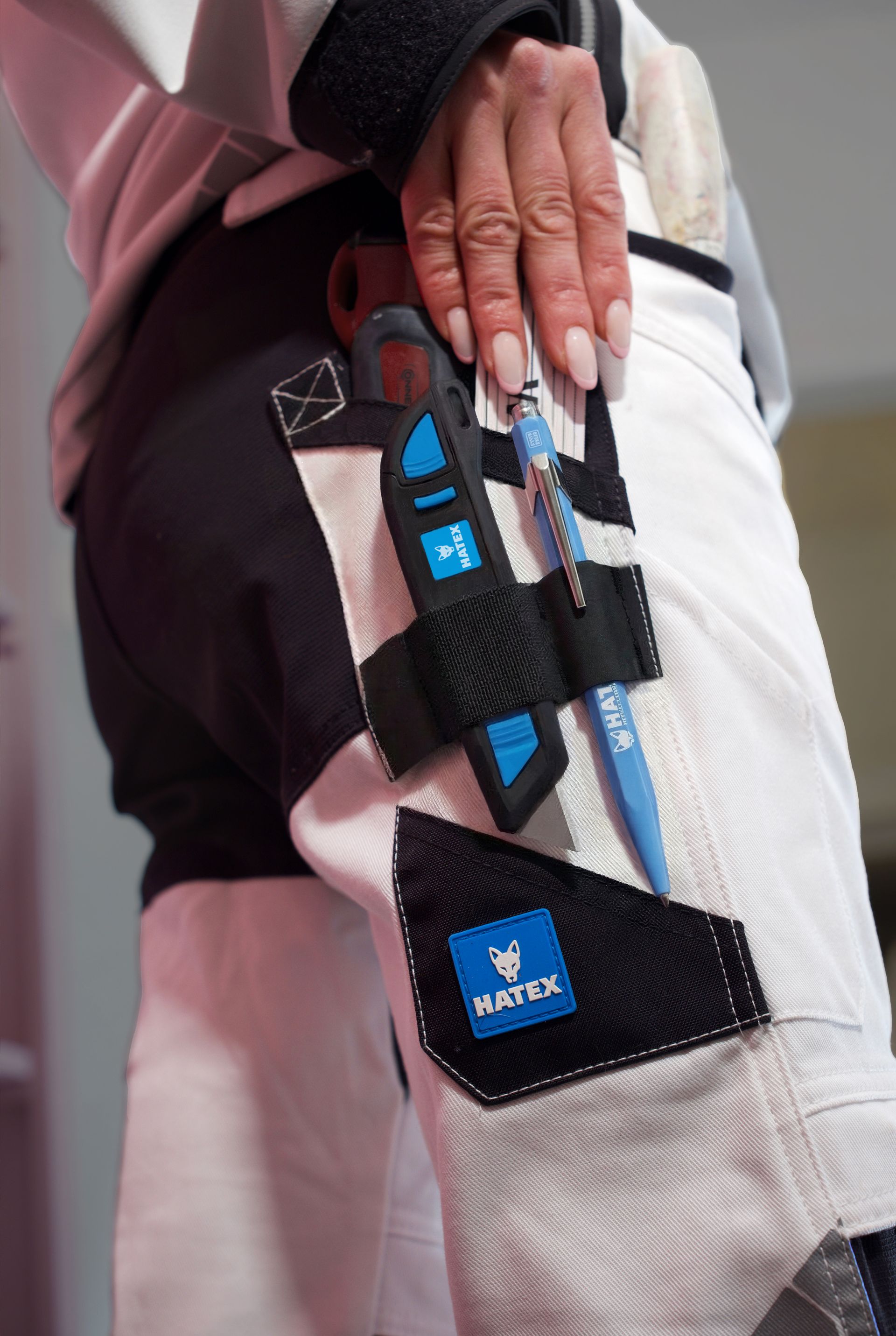 Nahaufnahme einer Hand, die einen weiß-schwarzen Anzug mit blauen Sicherheitsaufnähern und -gurten hält.