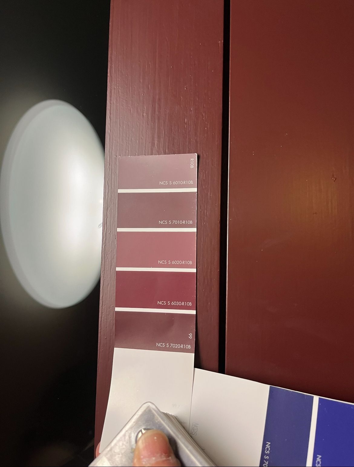 Eine Person hält ein Farbmuster neben einer Tür