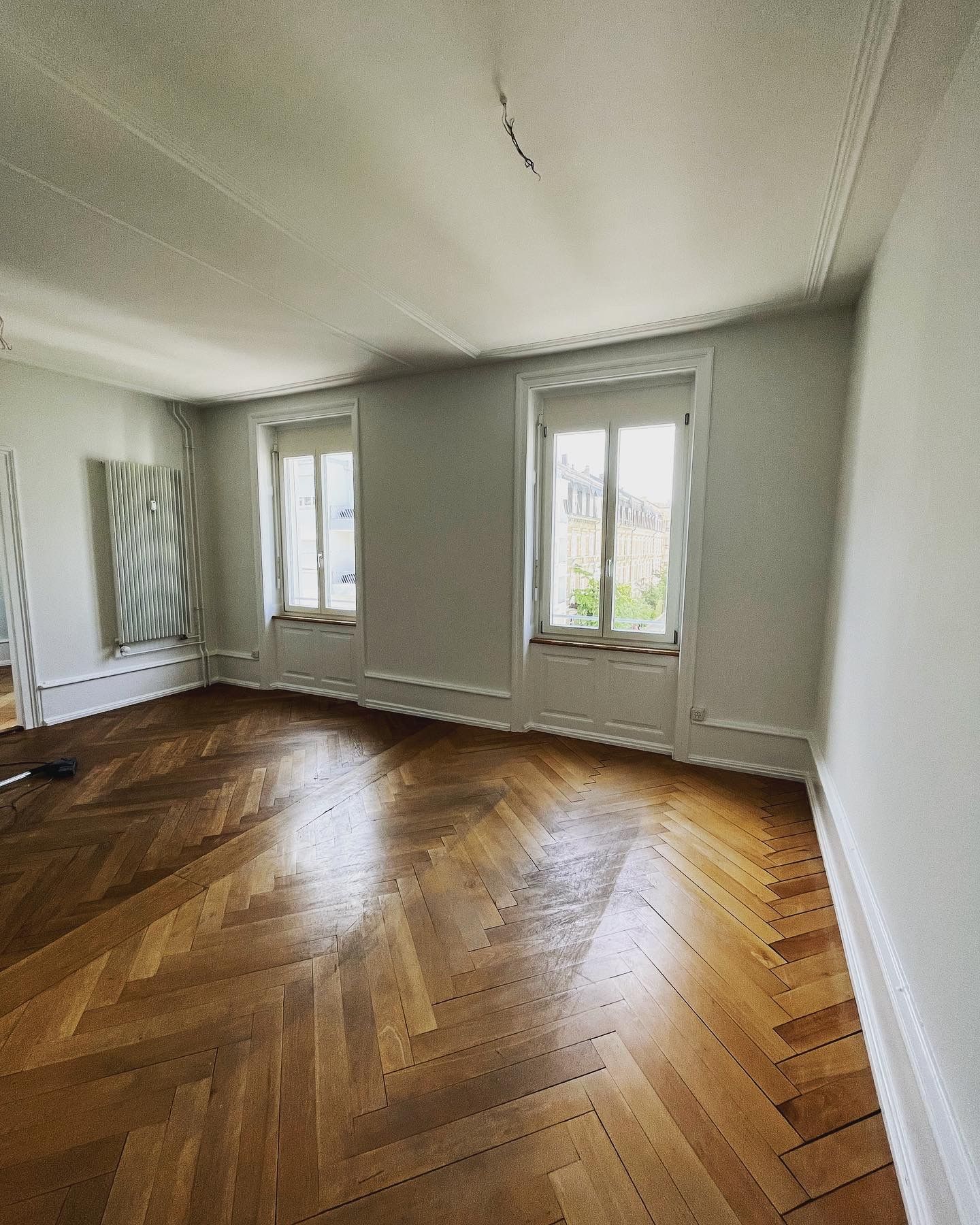 Ein leerer Raum mit Holzboden und zwei Fenstern.