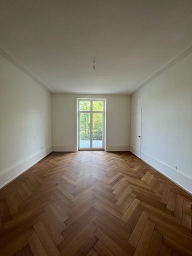 Ein leerer Raum mit Holzboden und großem Fenster.