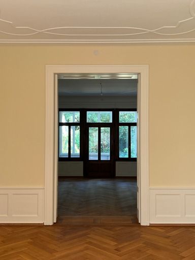 Ein leerer Raum mit Holzboden und einer Tür, die zu einem anderen Raum führt.