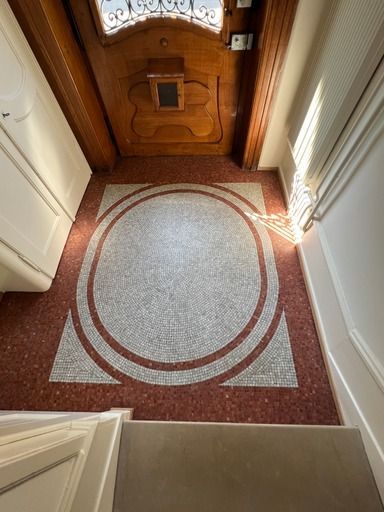 Ein Flur mit rot-weißem Fliesenboden und einer Holztür.