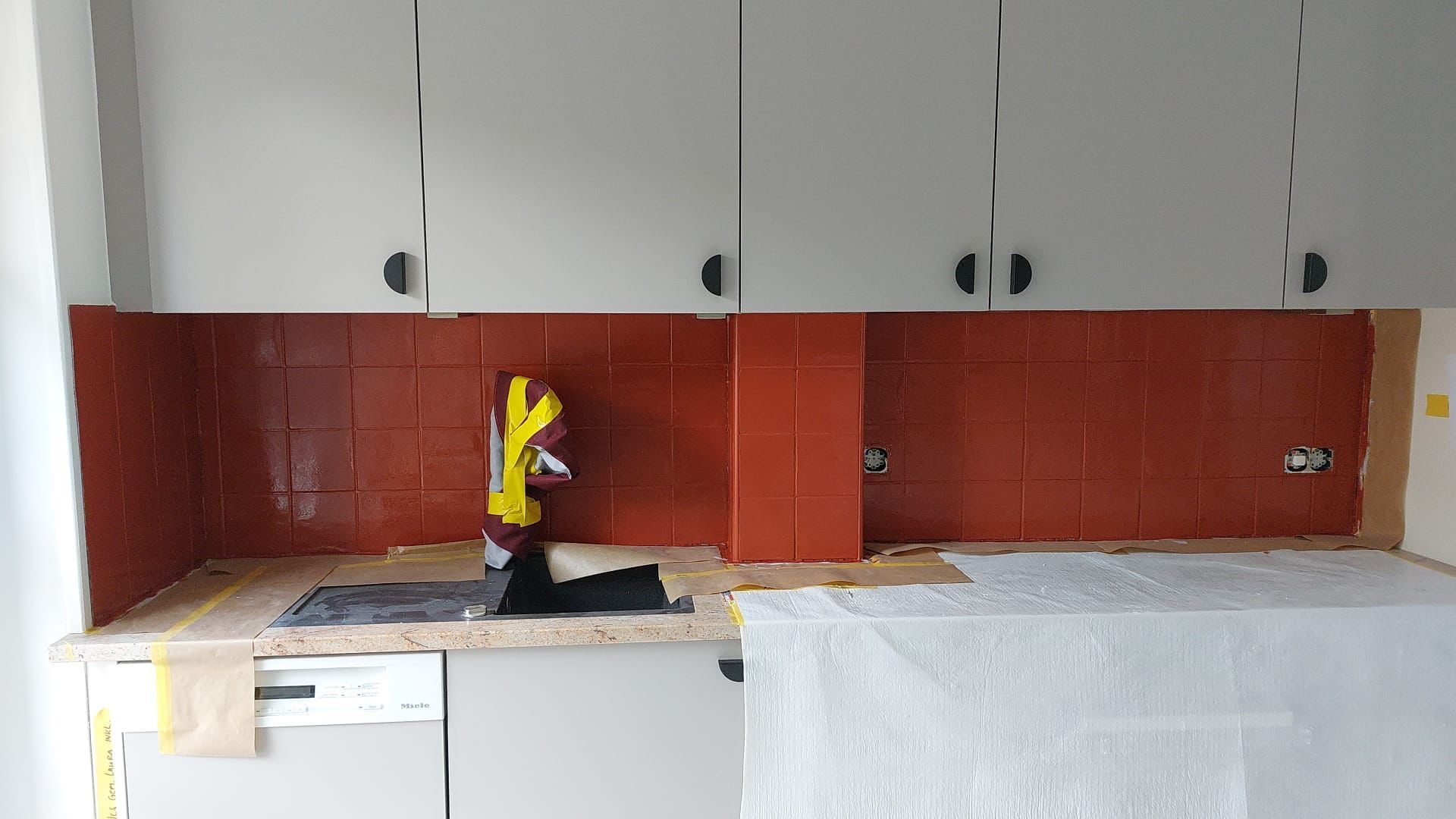 Eine Küche mit roten Fliesen und weißen Schränken und einer Sprühflasche auf der Anrichte.