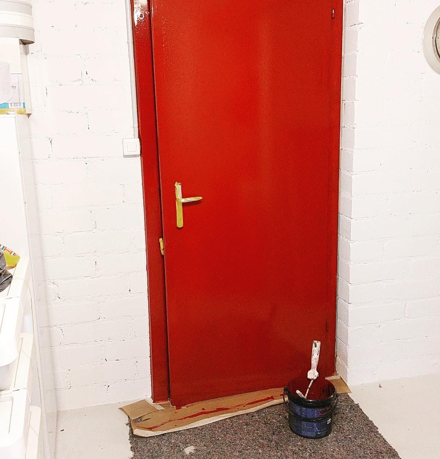 Eine rote Tür mit einem goldenen Griff befindet sich in einem Raum mit weißen Backsteinwänden.