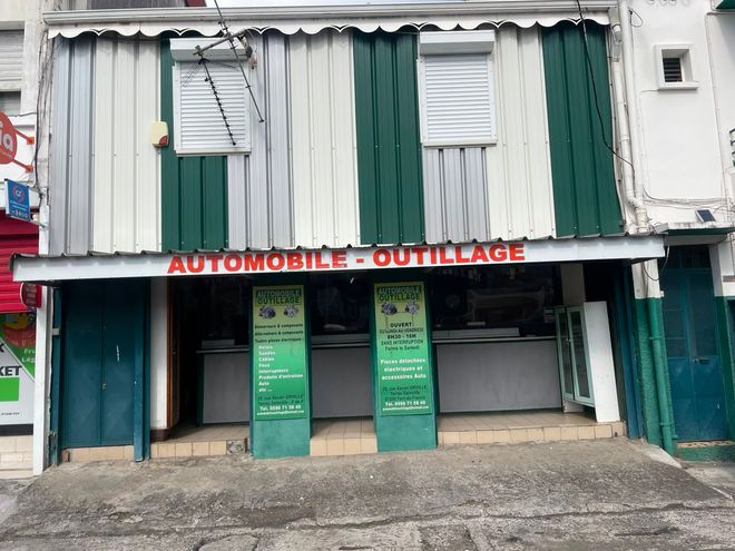 Magasin fermé avec volets verts et enseigne rouge « AUTOMOBILE OUTLAUGE » au-dessus de l'entrée