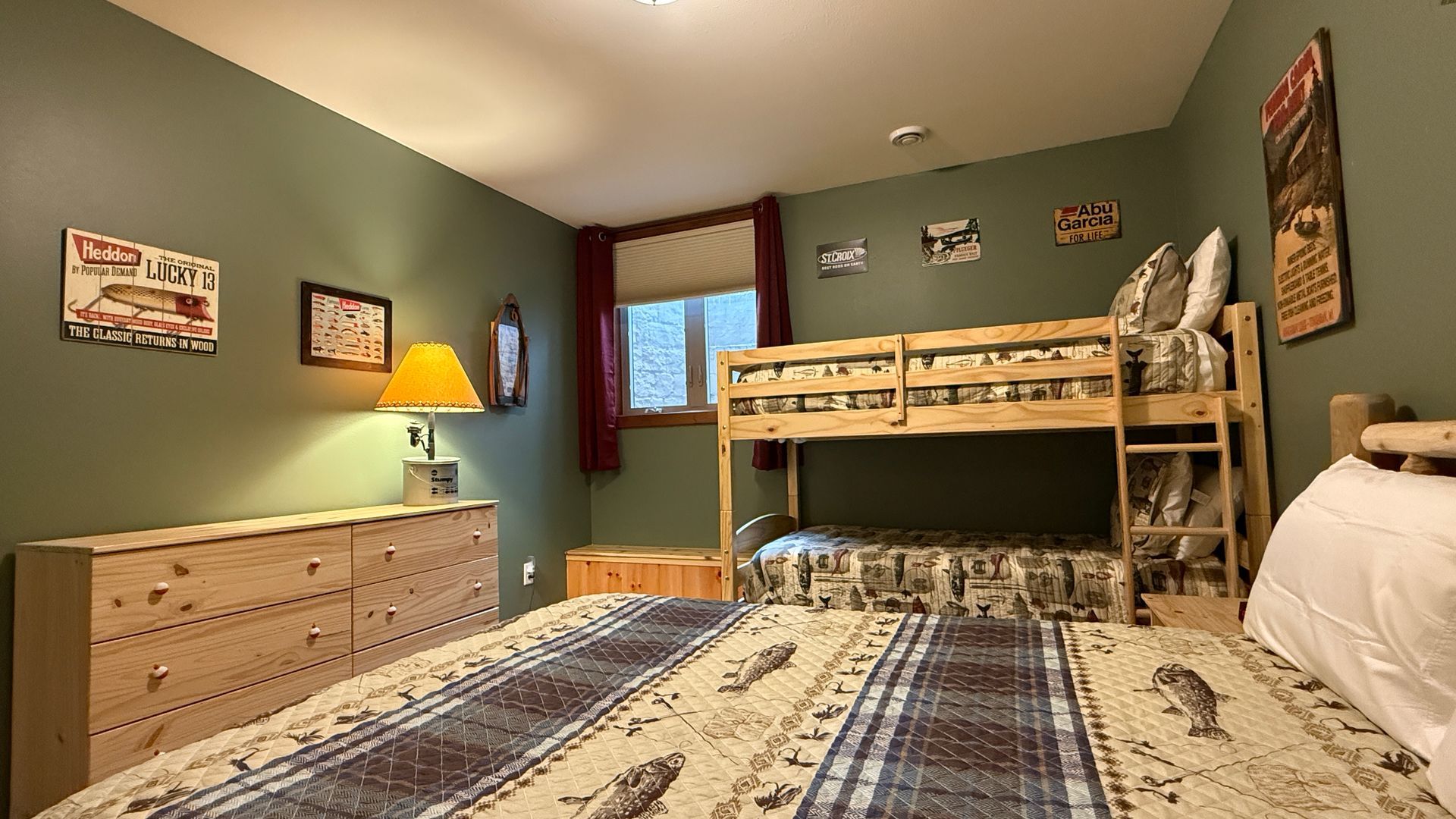 Bedroom with bunk beds, dresser, and a bed. Walls are green with fishing decor.