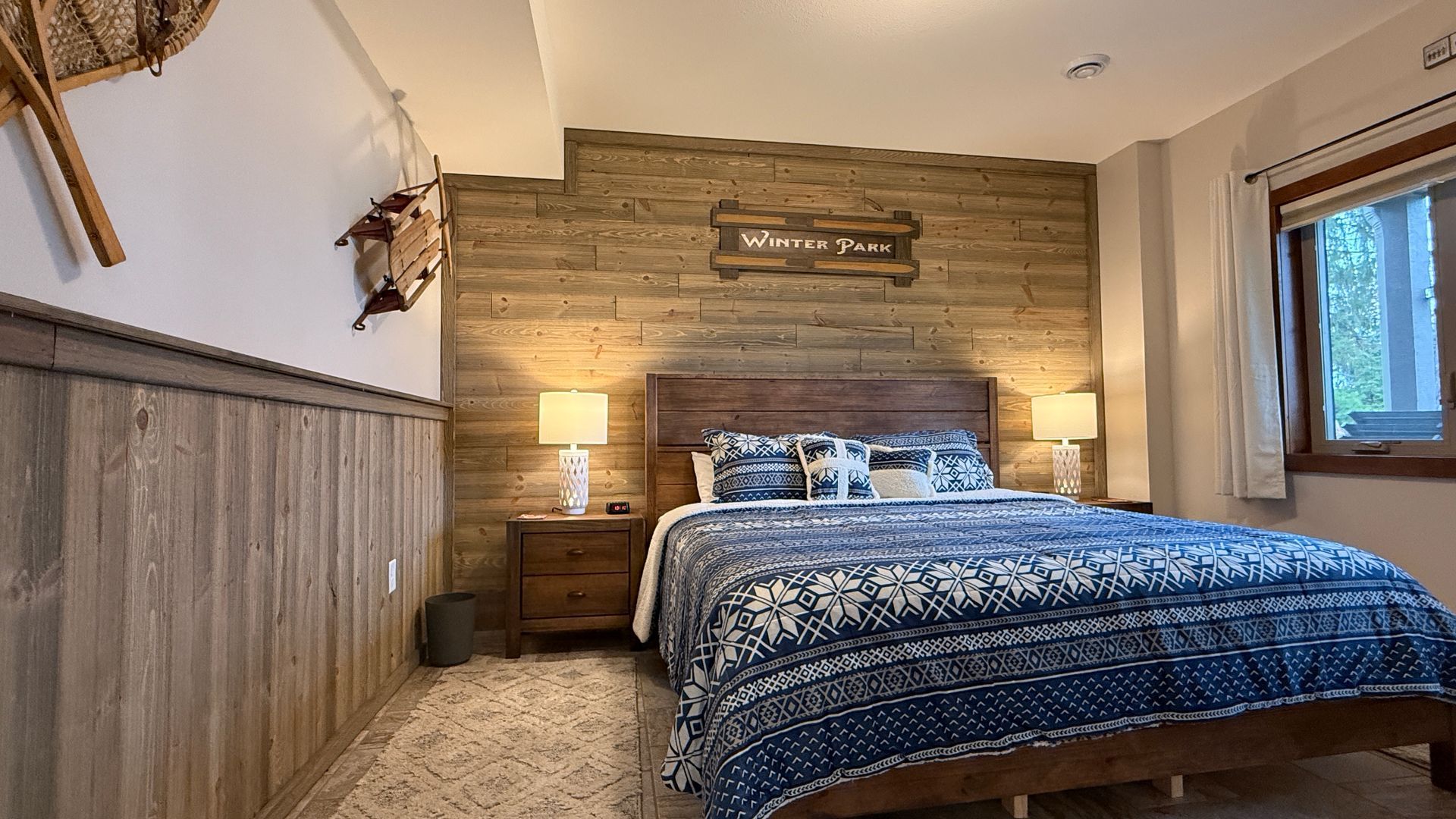 Bedroom with wood-paneled walls, a bed with blue bedding, and a small window.