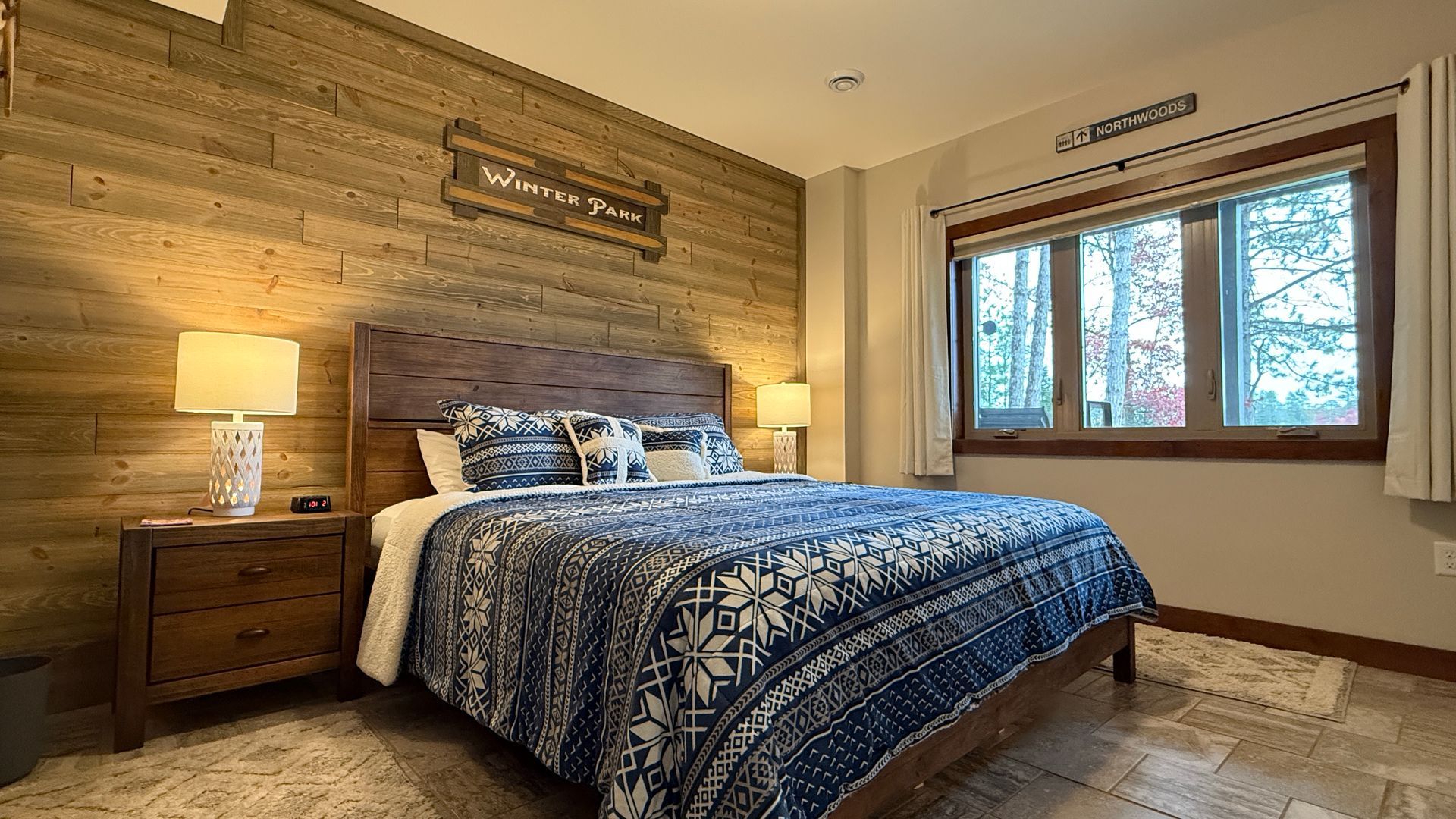 Cozy bedroom with wooden accent wall, a bed with blue patterned quilt, nightstands, and a window.