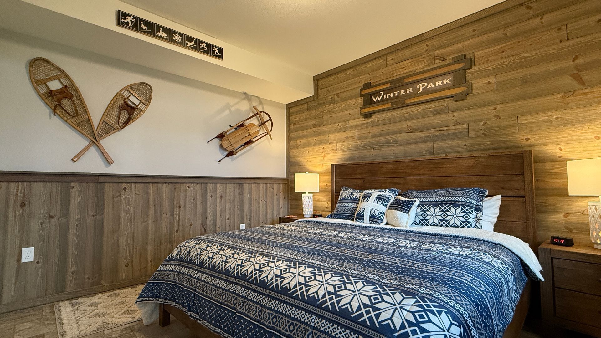 Bedroom with rustic wood paneling, a bed with blue snowflake bedding, and snowshoes on the wall.
