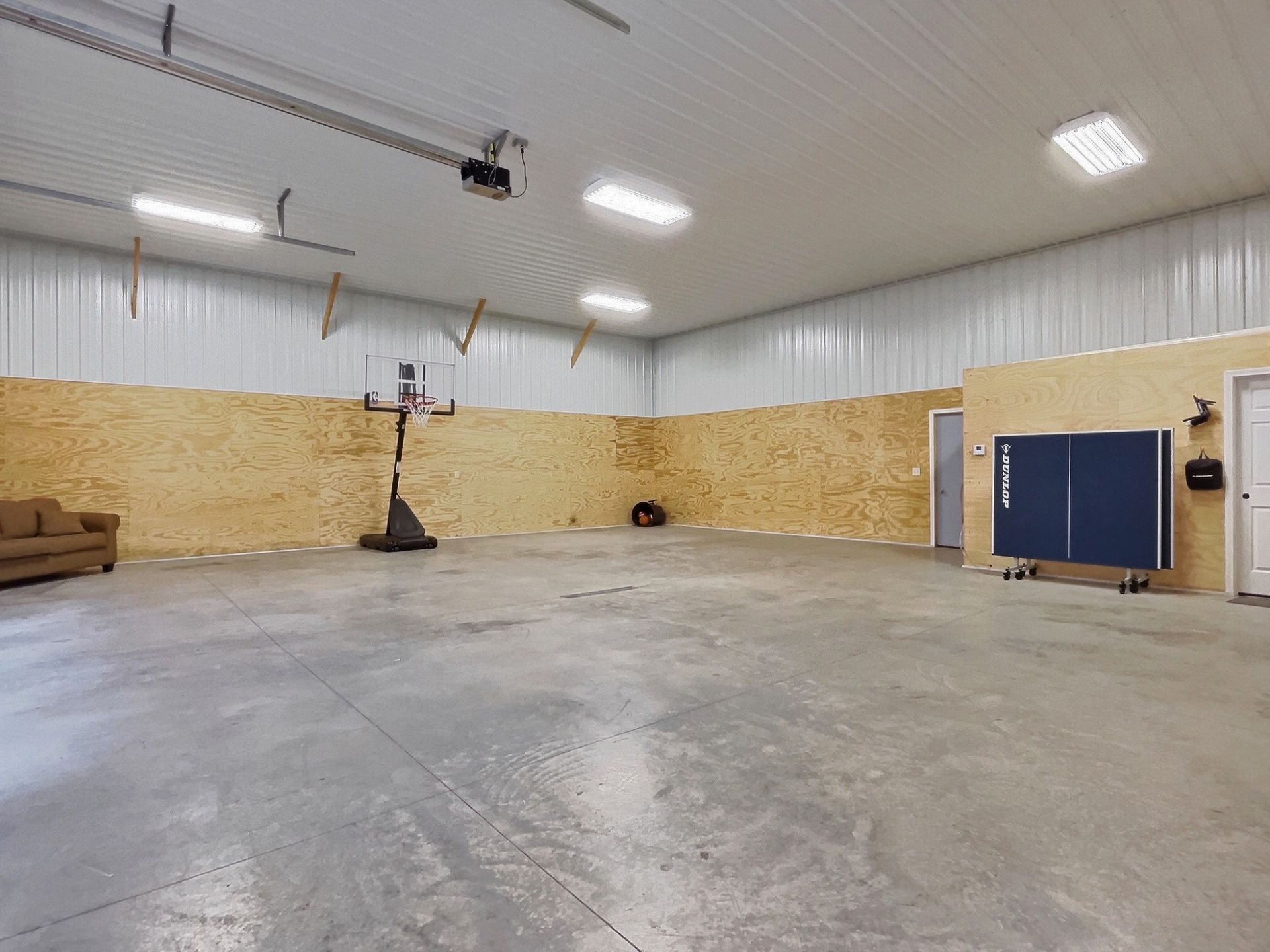 Large open room with concrete floor, basketball hoop, ping pong table, and tan walls.