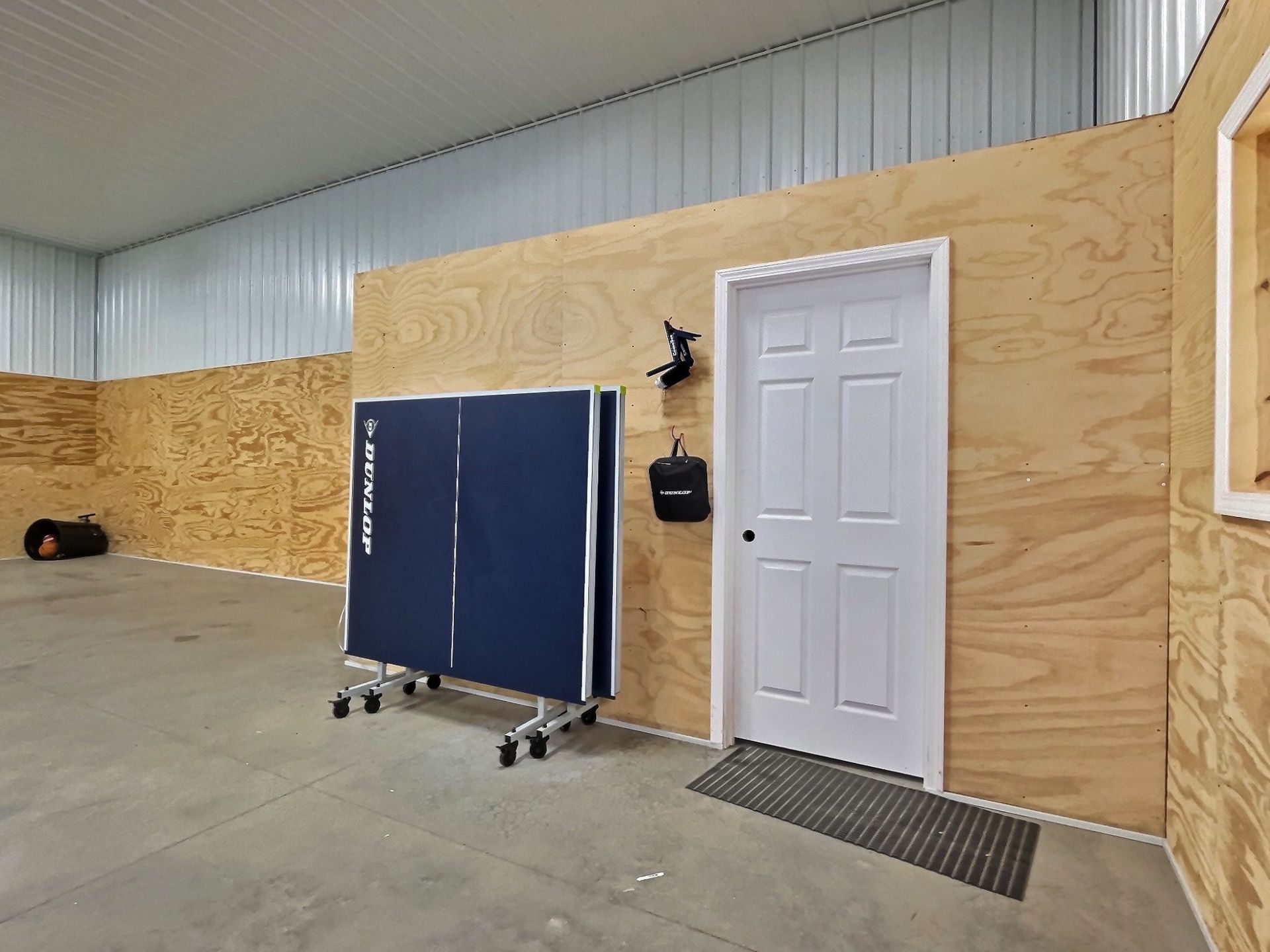 Ping pong table in a room with plywood walls and a white door.