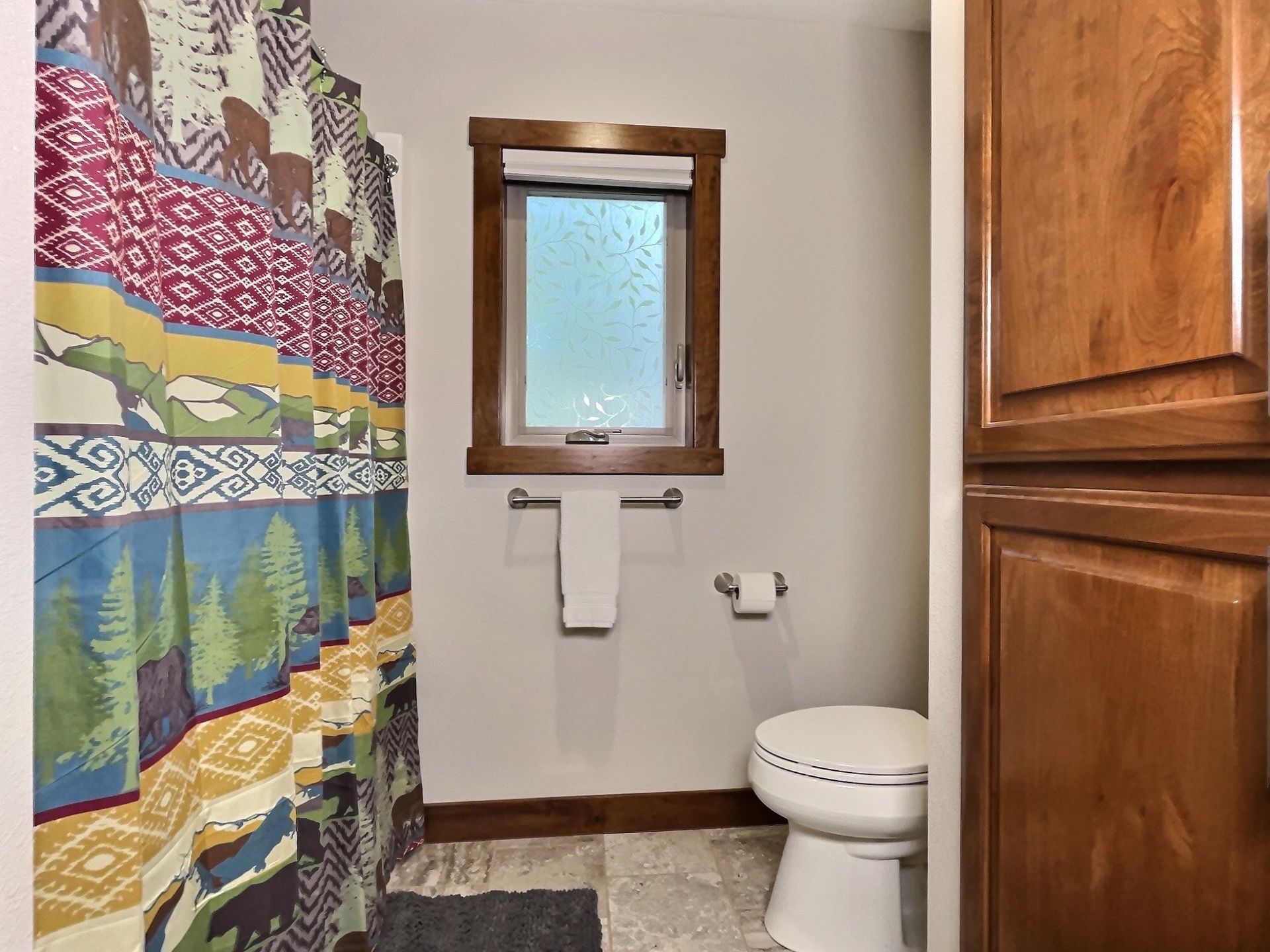 Bathroom with shower curtain, toilet, window, and wood cabinetry.