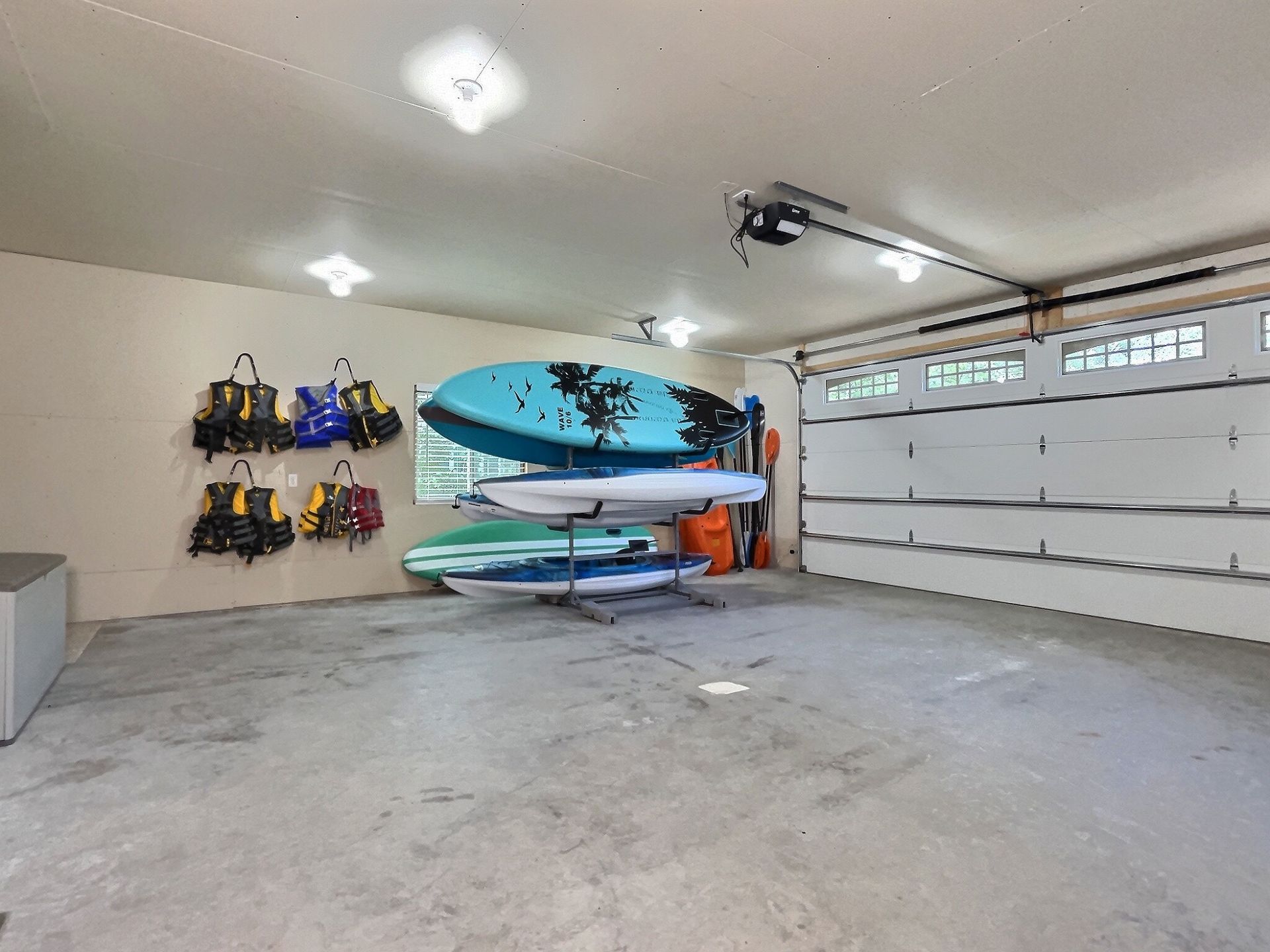 Garage interior with paddleboards, life vests, and a garage door.