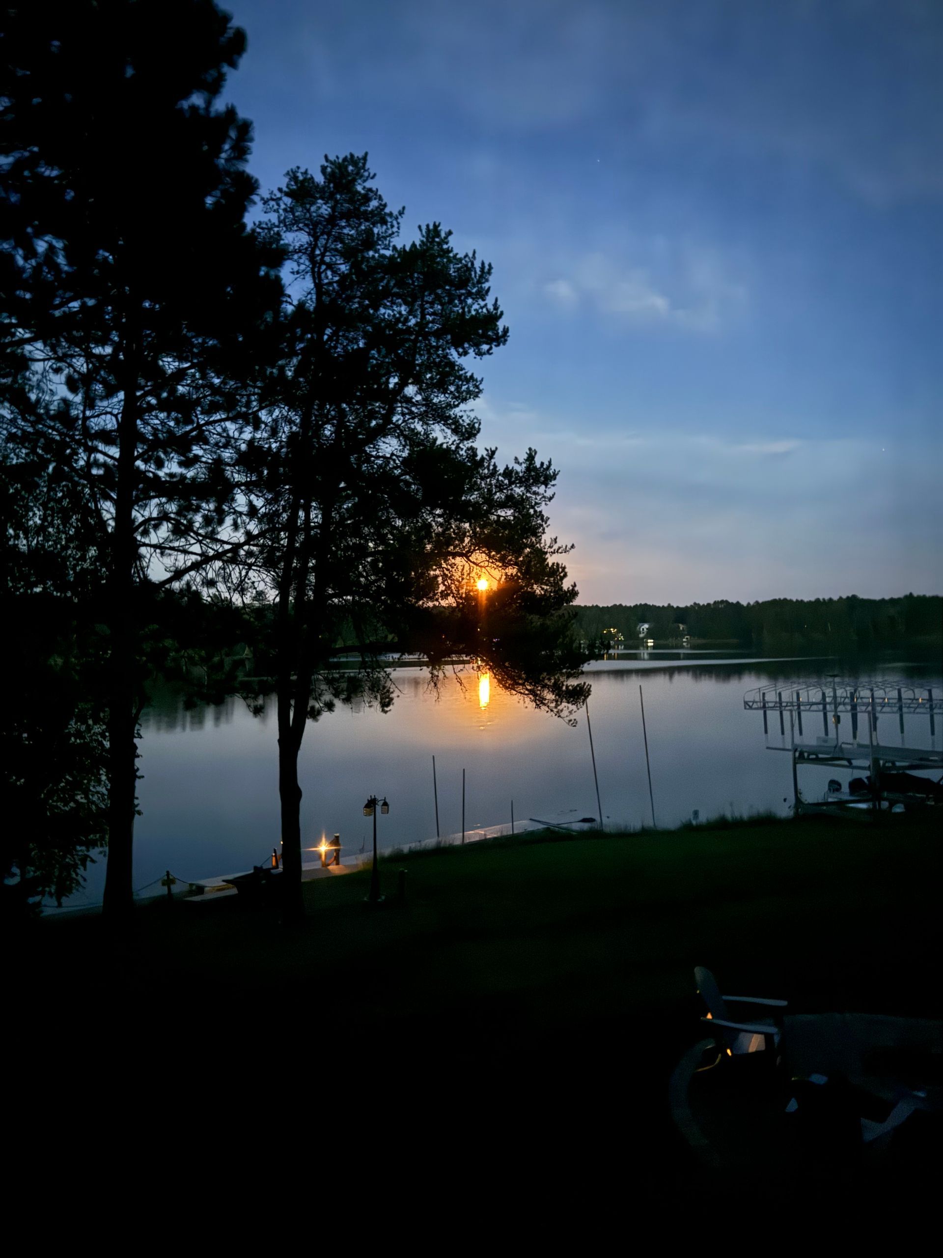 Lake scene at dusk, with trees silhouetted against the water, reflecting the setting sun.