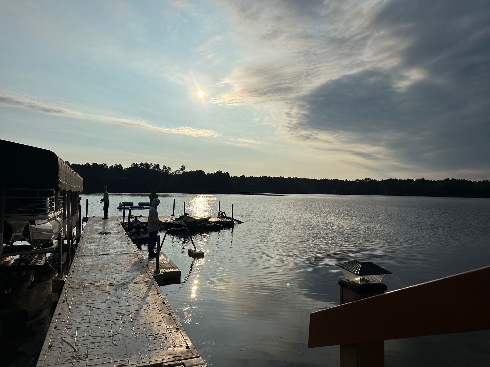 Dock overlooking calm water reflecting sunlight, under a cloudy sky.