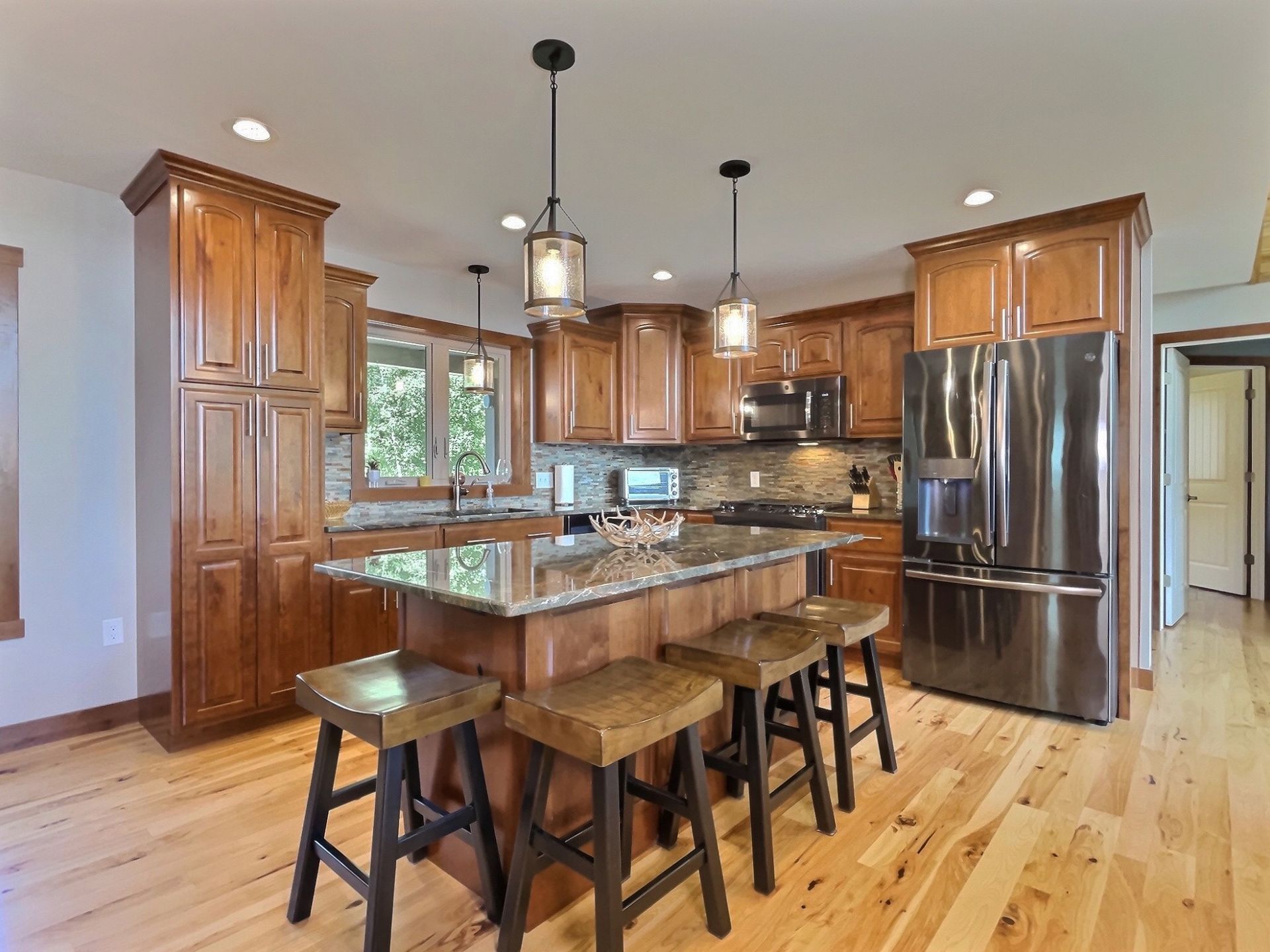 Kitchen with wood cabinets, island with stools, stainless steel appliances, and wood flooring.