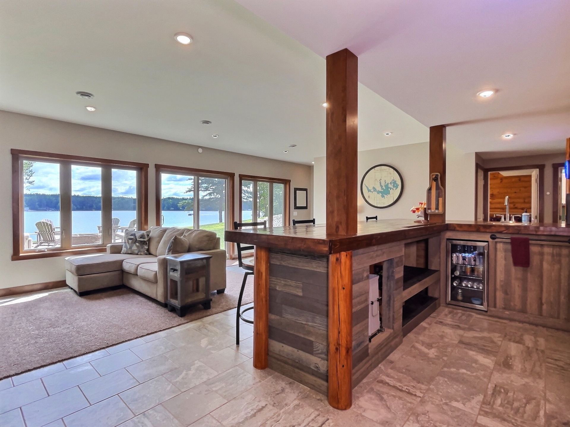 Living area with lake view, sectional sofa, bar with rustic wood, and a mini-fridge.