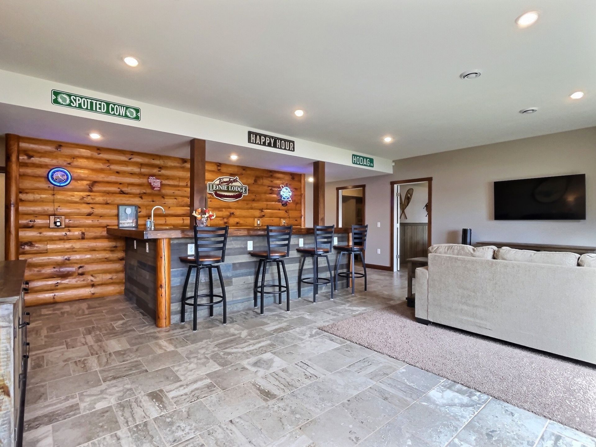 Basement bar with log-style wall, seating, and a mounted TV.