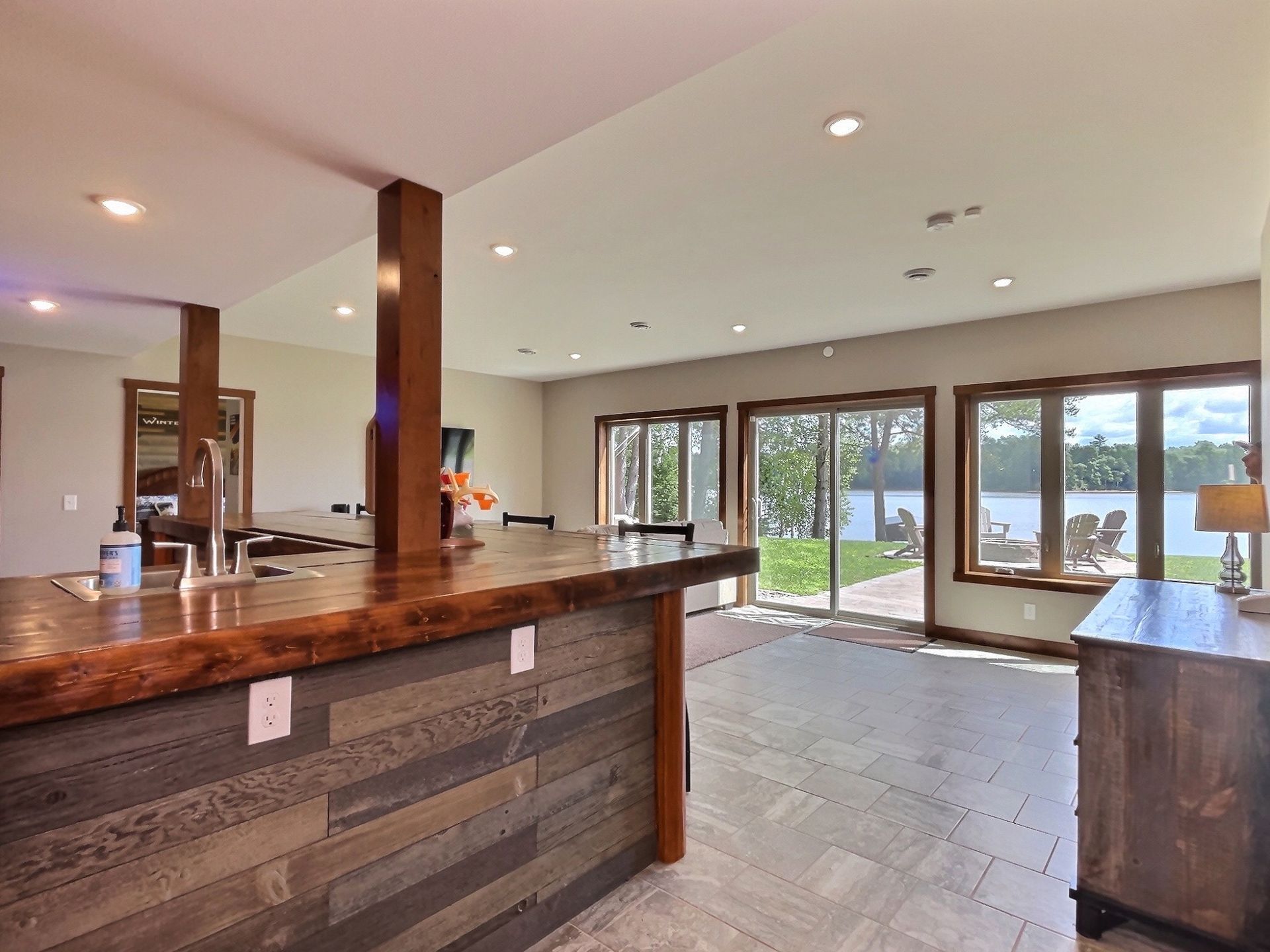 Spacious room with a rustic bar, opening to a lakeside view through sliding glass doors.