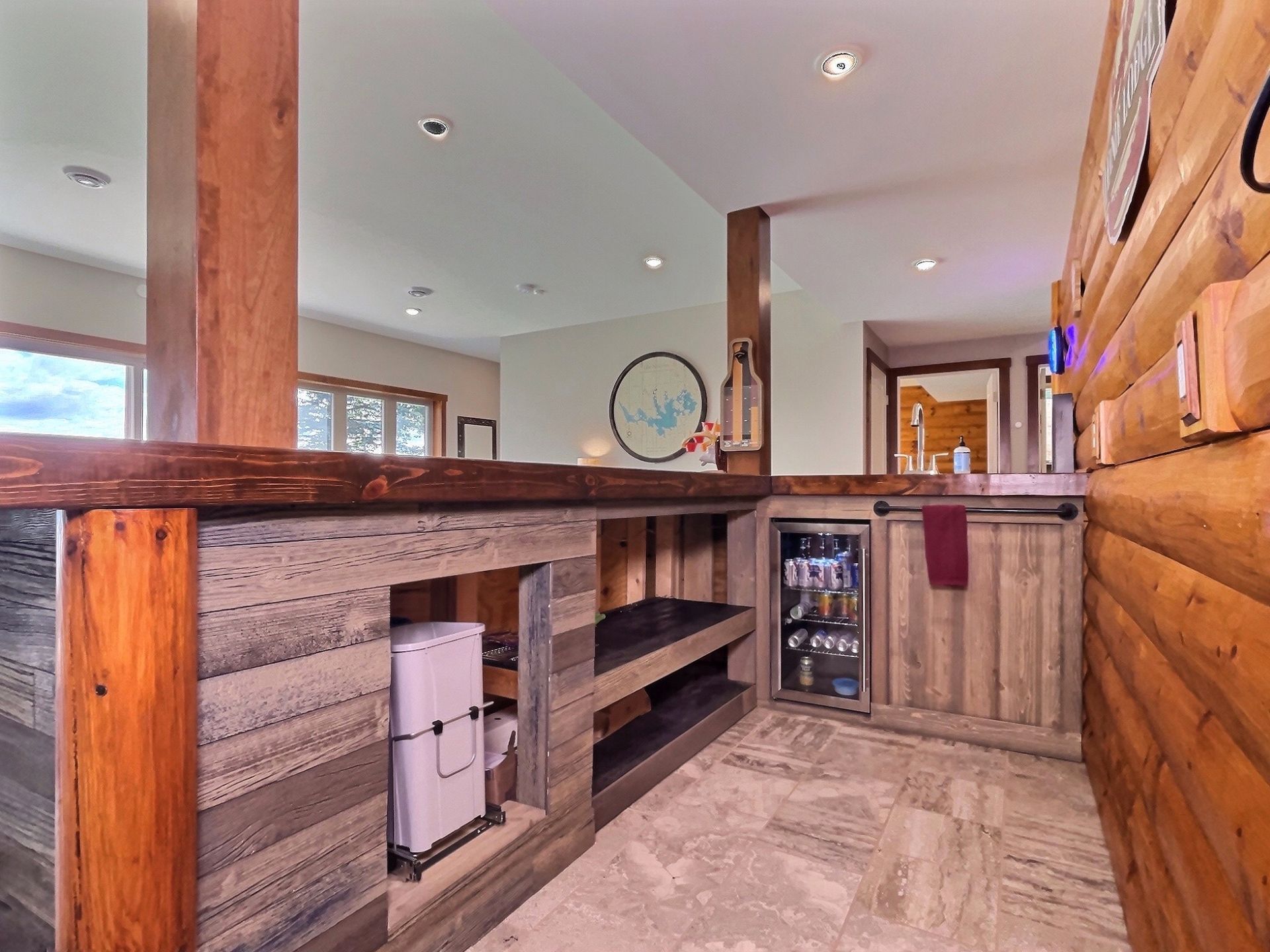 Rustic bar area with log and wood detailing, cooler, mini-fridge, and built-in shelving.