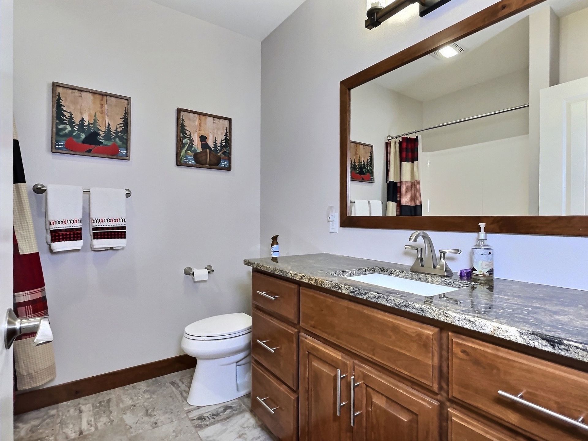 Bathroom with a wooden vanity, granite countertop, and framed mirror. Red and white towels on the wall.