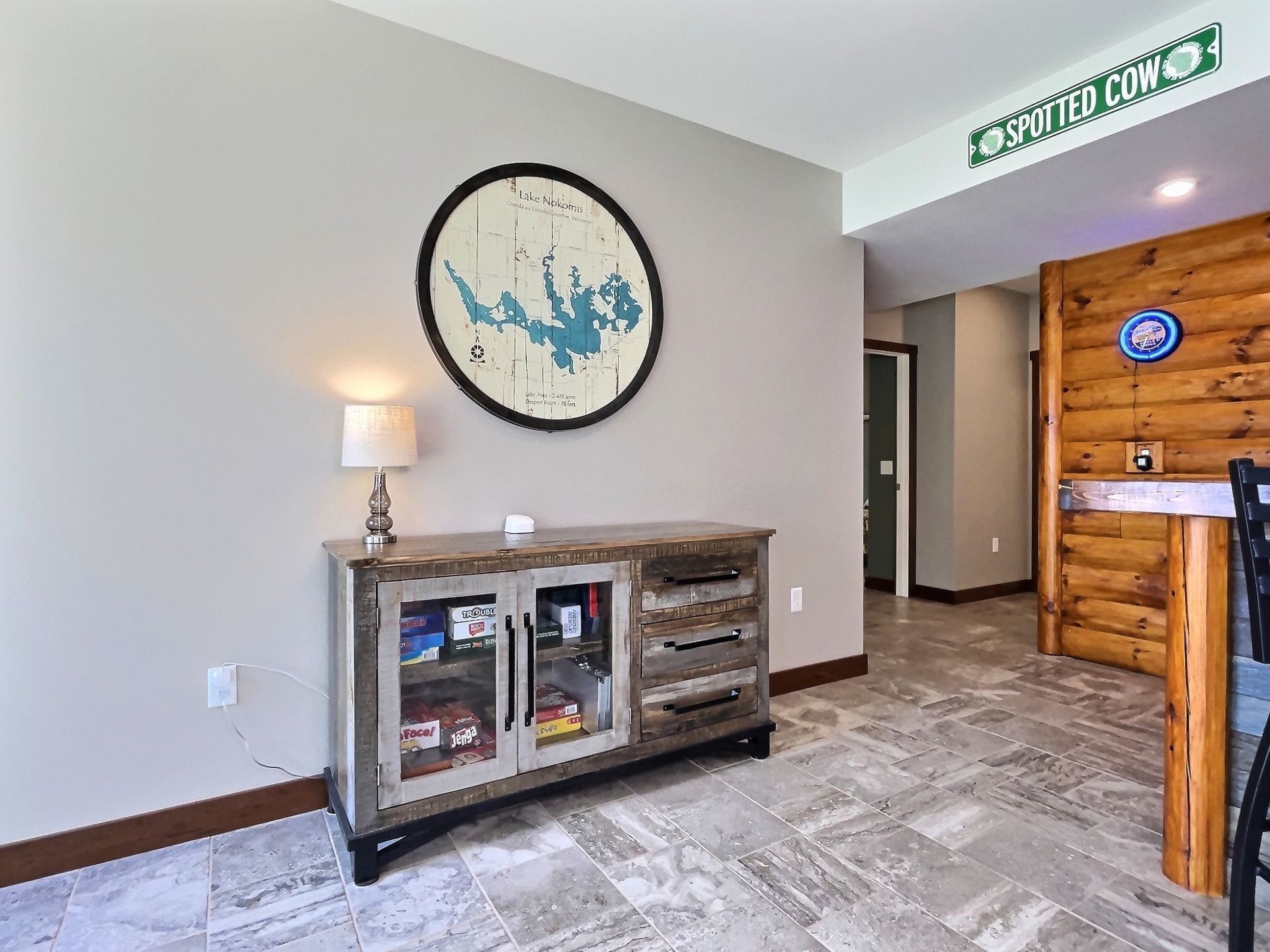 A wooden cabinet with a lamp and a circular lake map. A log-style bar is to the right.