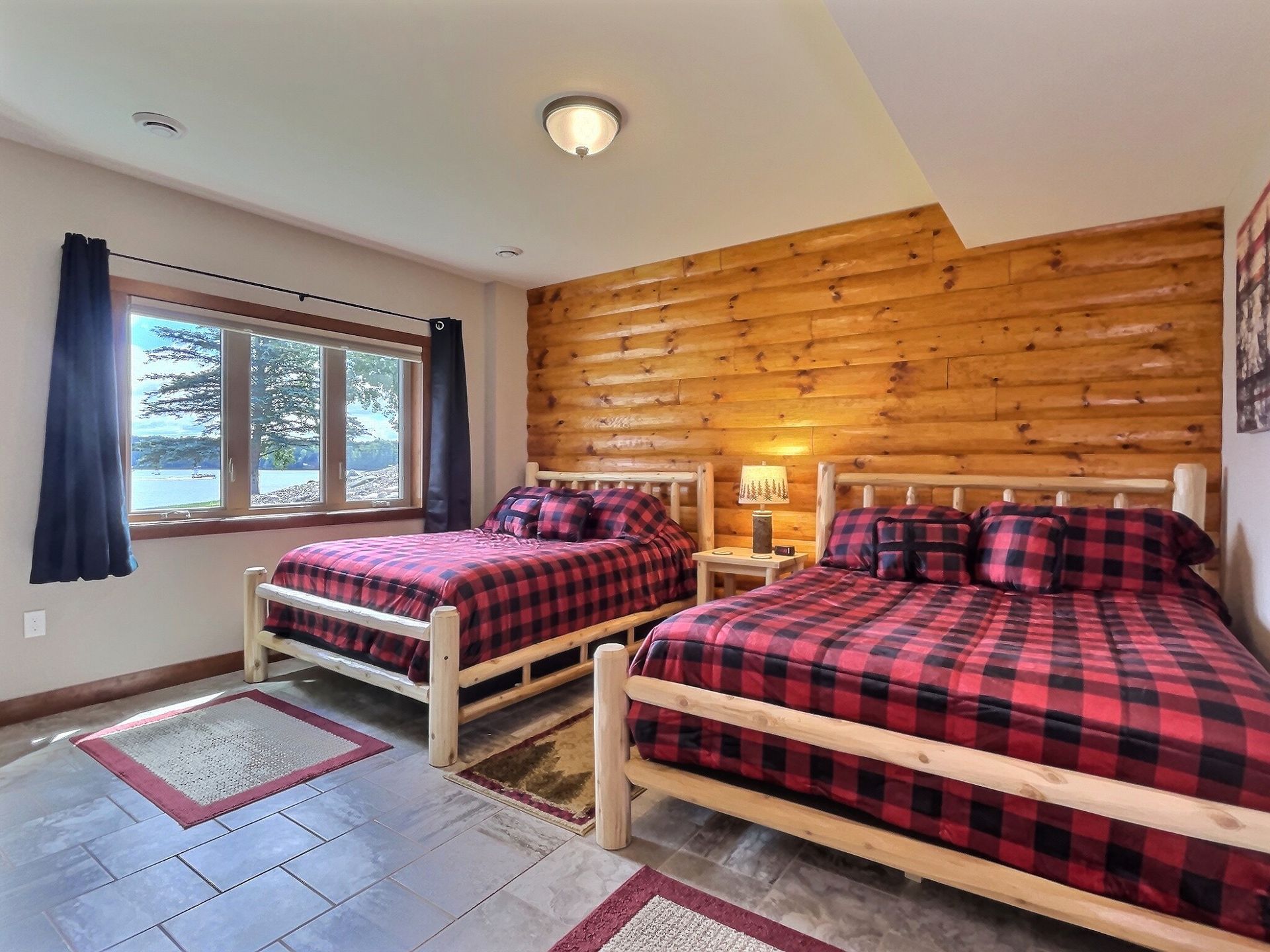 Bedroom with two queen beds, red plaid bedding, log-style wall, window with lake view.