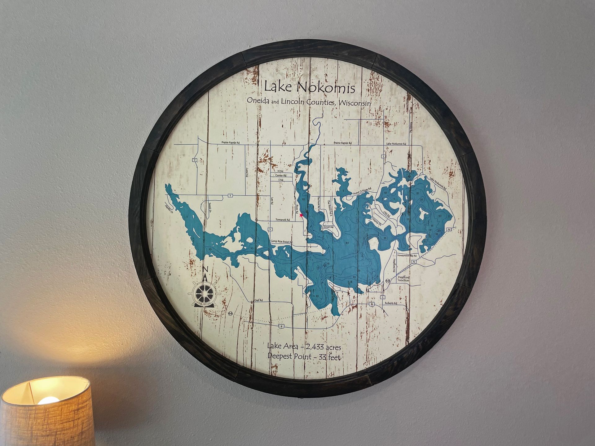 Round map of Lake Nipigon in blue and white, framed in black, hanging on a gray wall.