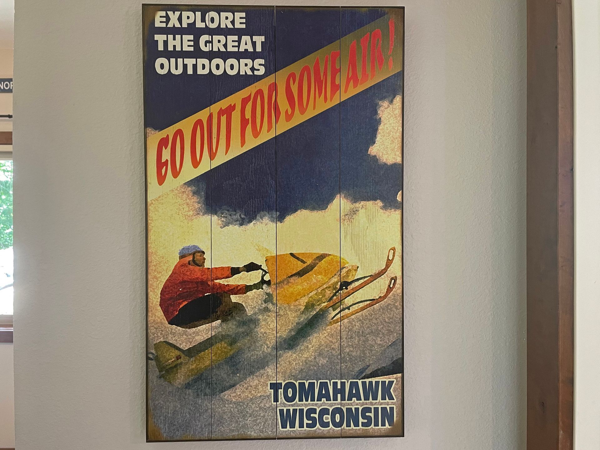 Poster: Man on a snowmobile, yellow and orange, in snowy scene. 