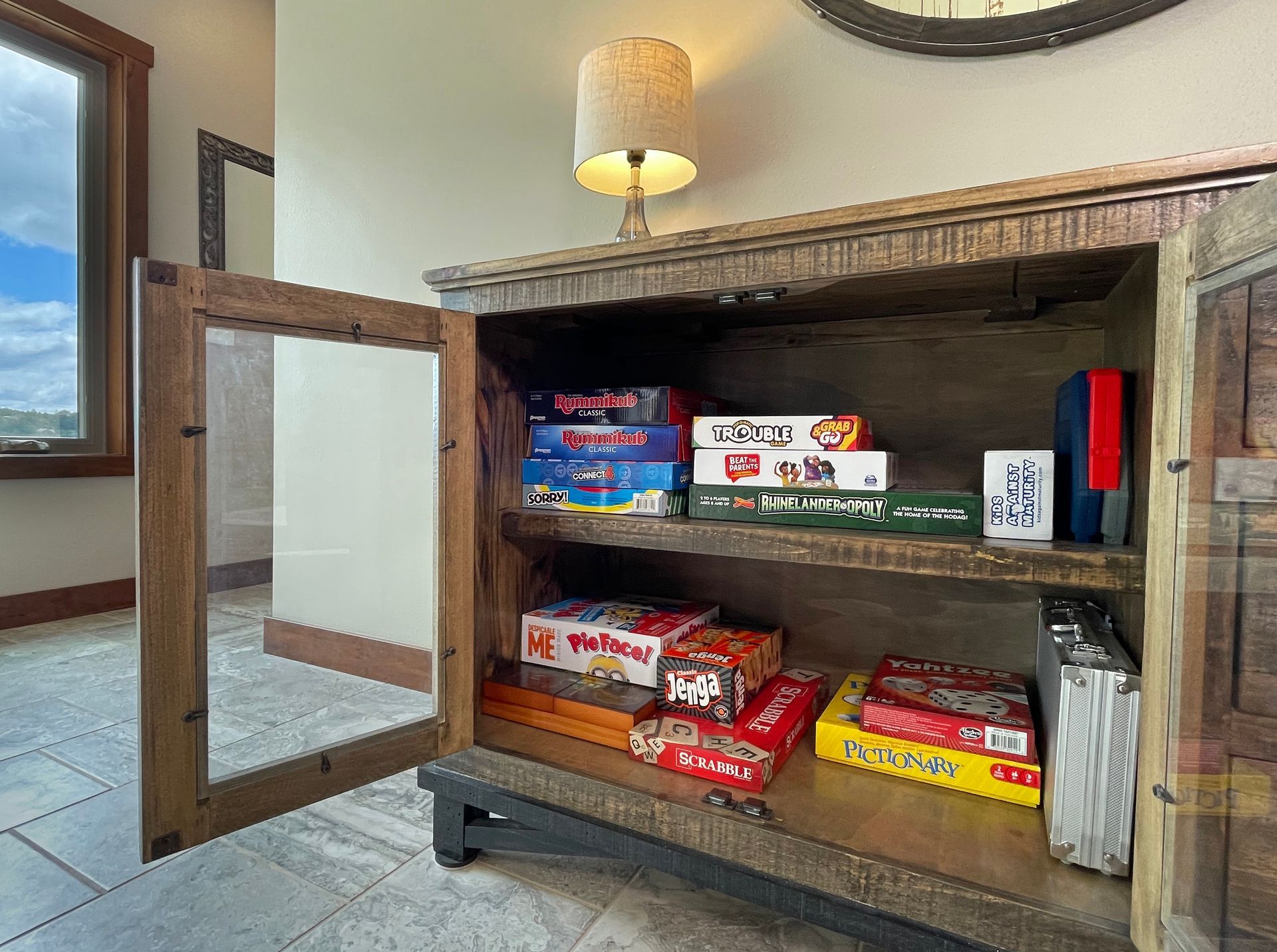 Wooden cabinet with games on shelves; open glass door.